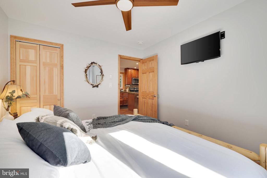 Bedroom with a white bed, gray pillows, wooden doors, ceiling fan, and wall-mounted television.
