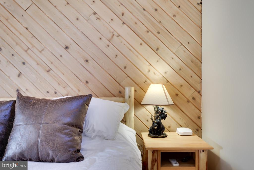 Bedroom with a wood-plank sloped wall, white bedding, and a lit bedside lamp.