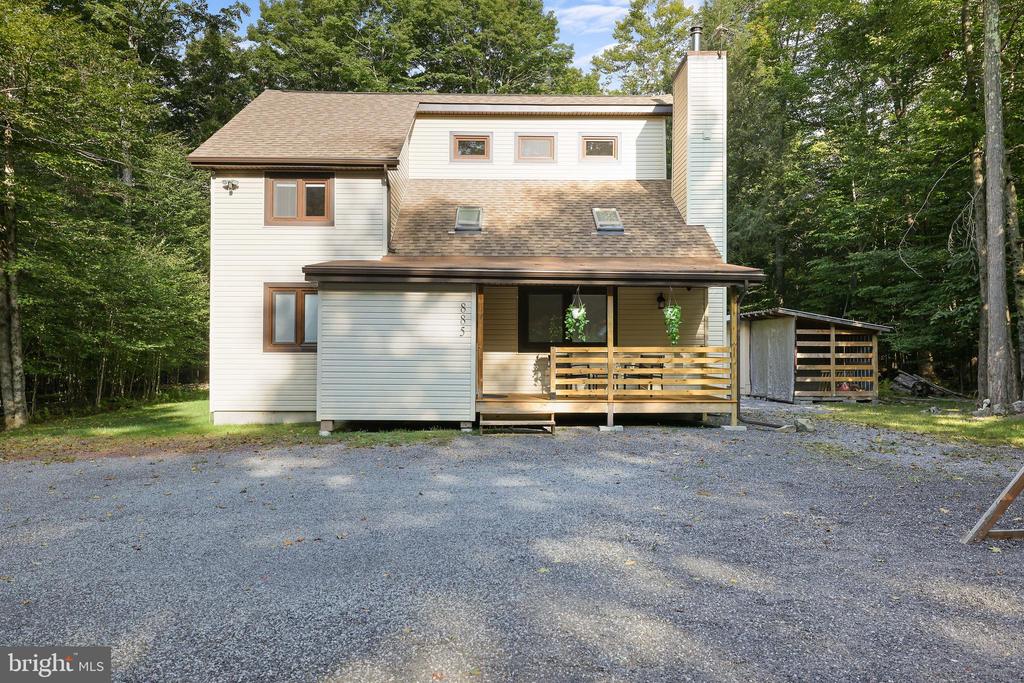 Two-story house with a covered porch and gravel driveway, surrounded by trees.