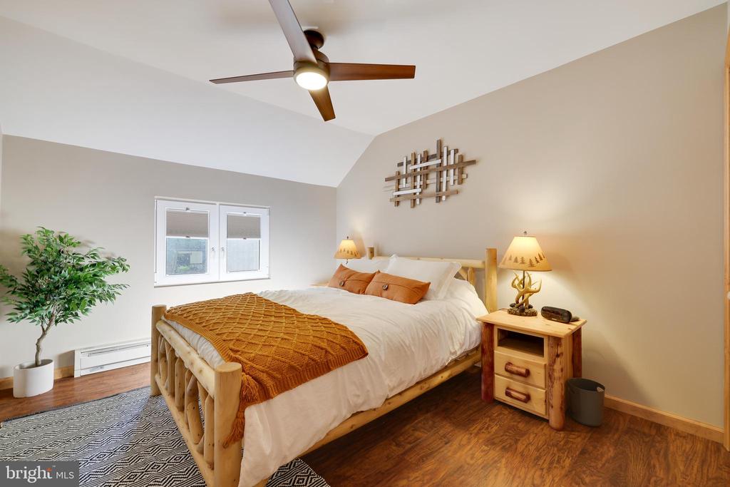 Furnished bedroom with a log-style bed, rust-colored throw, vaulted ceiling, and hardwood floors.