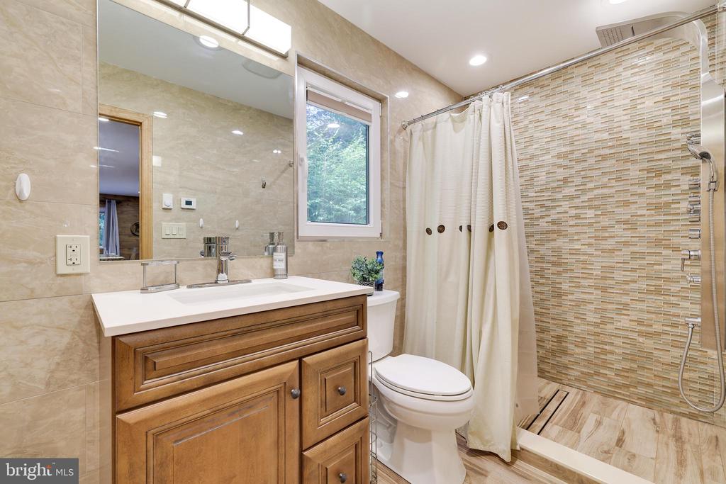 Bathroom with a wood vanity, beige mosaic-tile shower, and window.