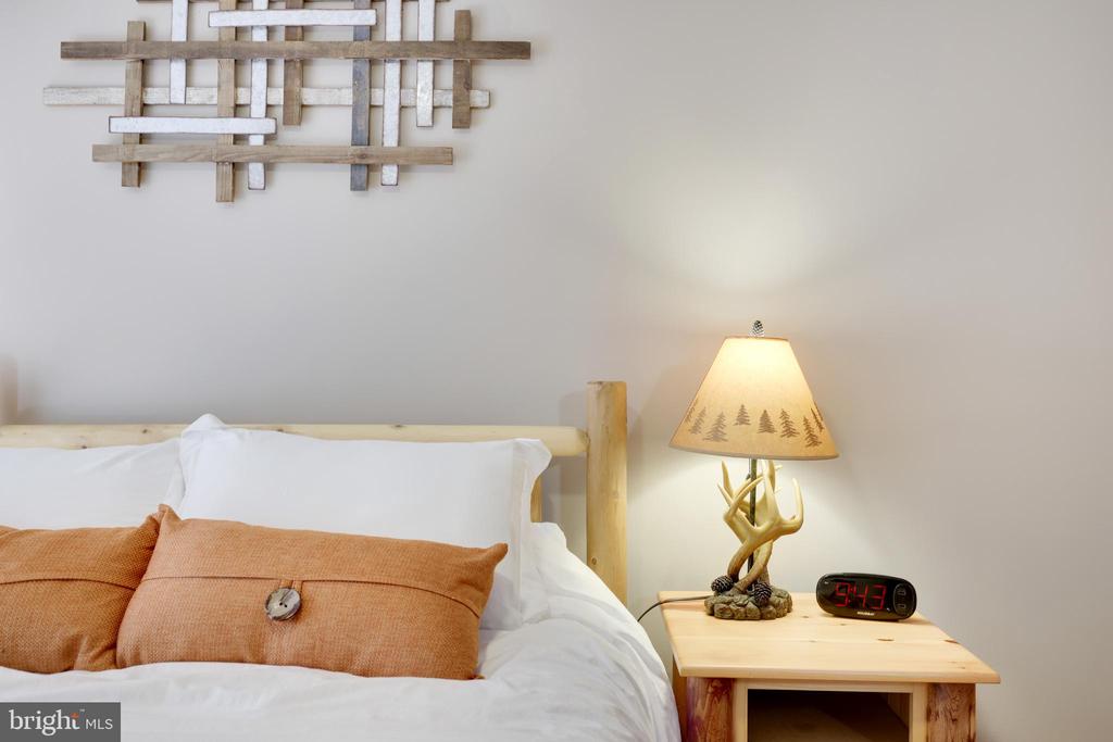 Bedroom with white bedding, rust-colored pillows, and a lit antler-base lamp on a pine nightstand.