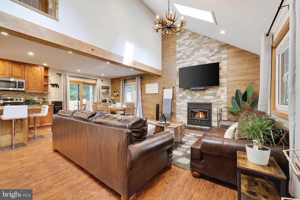 Open-plan living room with vaulted ceiling, stone fireplace, wood floors, and brown leather seating.