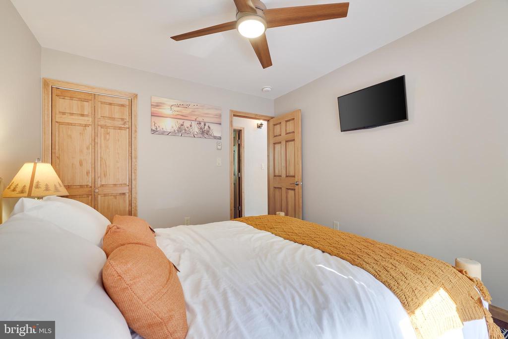 Bedroom with white bedding, an orange knit throw, wooden closet doors, and a ceiling fan.