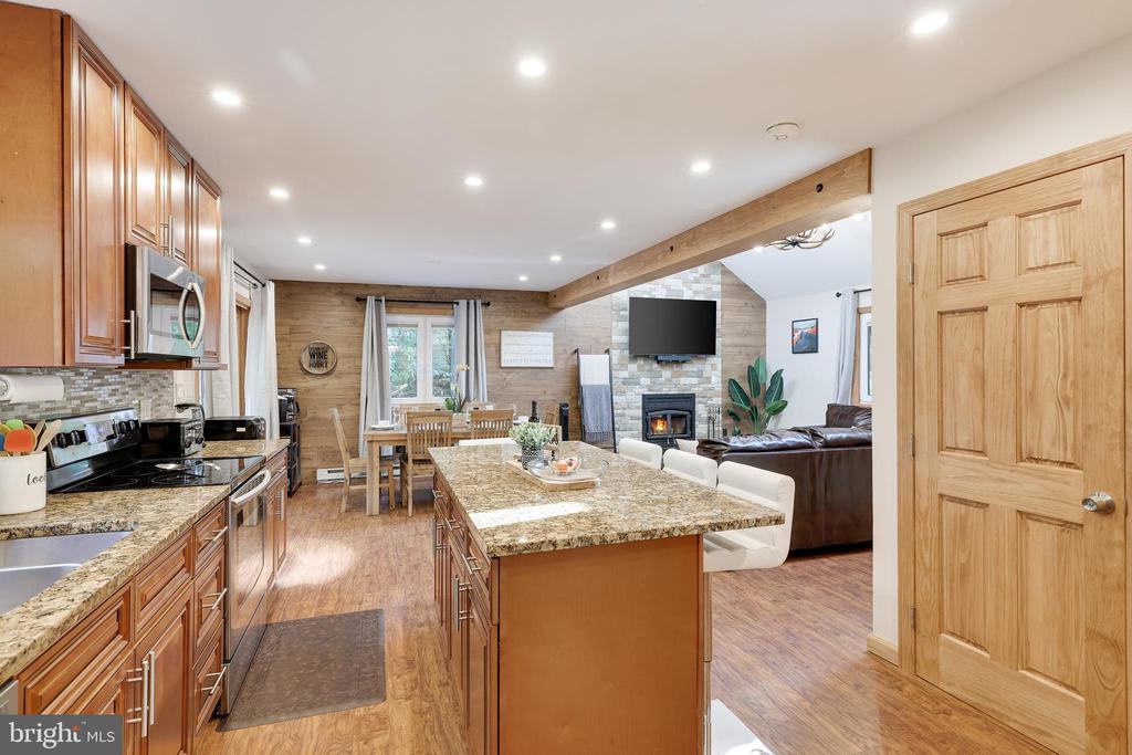 Open-plan kitchen with granite island, wood cabinetry, dining table, and living room fireplace.