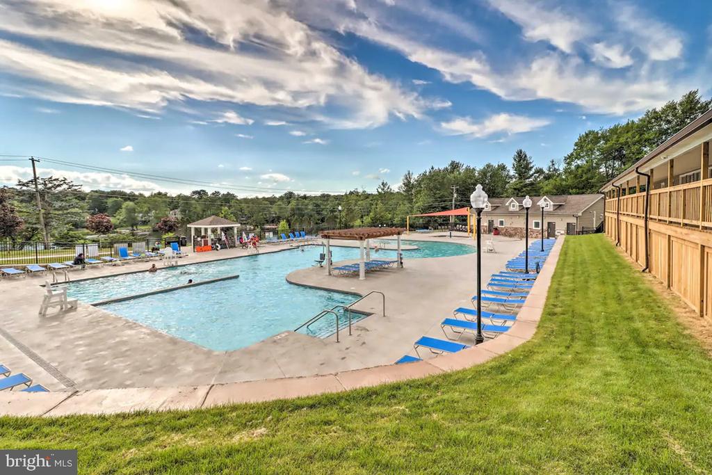 Community swimming pool with blue lounge chairs, a gazebo, and wooded surroundings.