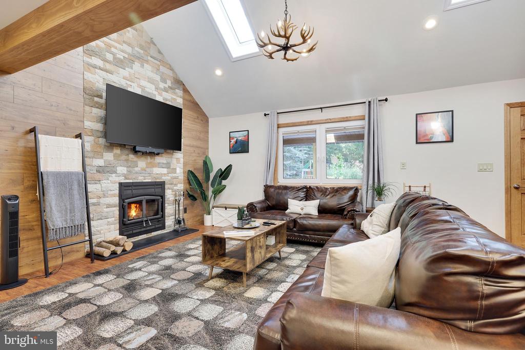 Living room with a stone fireplace, mounted television, leather sofas, and vaulted wood-beam ceiling.