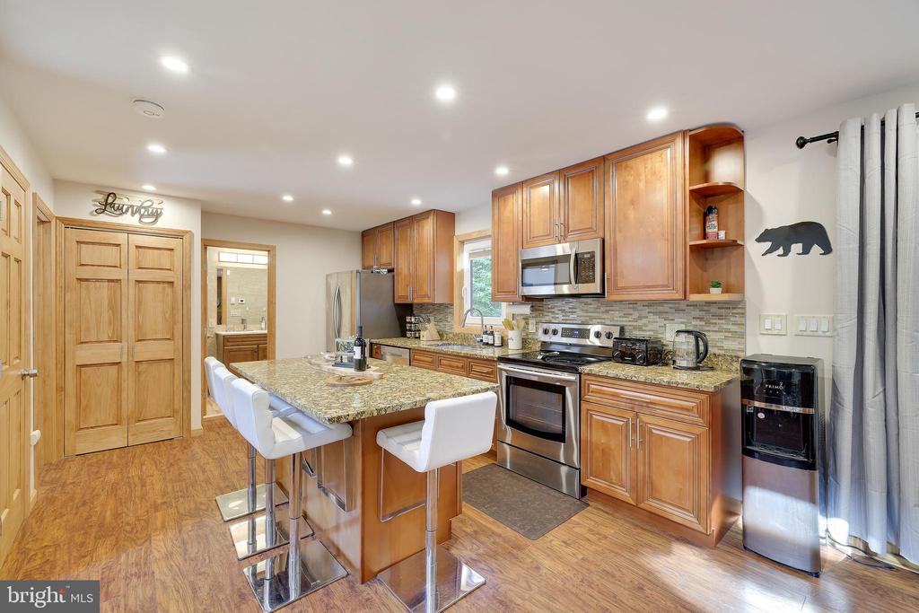 Kitchen with warm wood cabinets, stainless steel appliances, and a granite island with white stools.