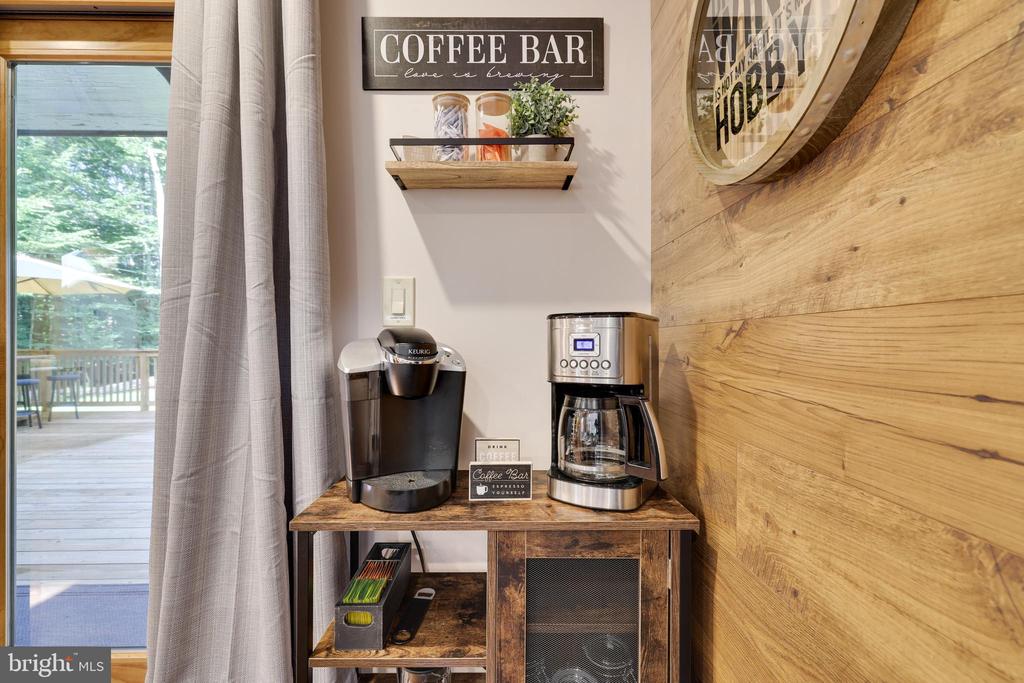 Coffee bar with two coffee makers beside a glass door opening onto a wooded deck.