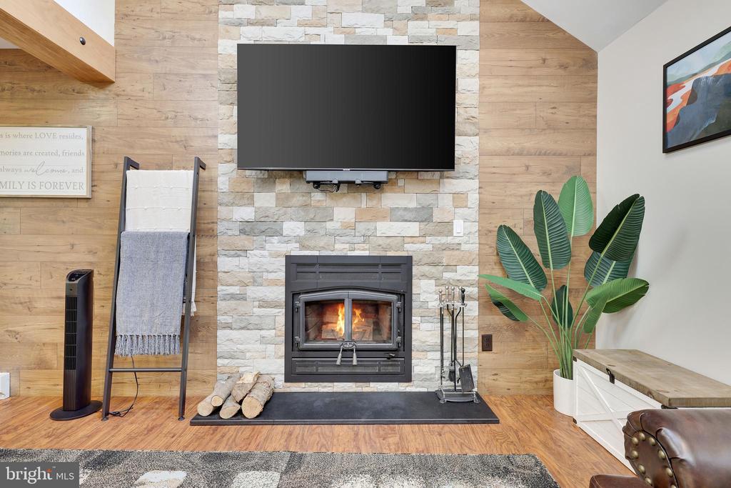Living room with a lit stone fireplace, wall-mounted television, and wood-paneled walls.