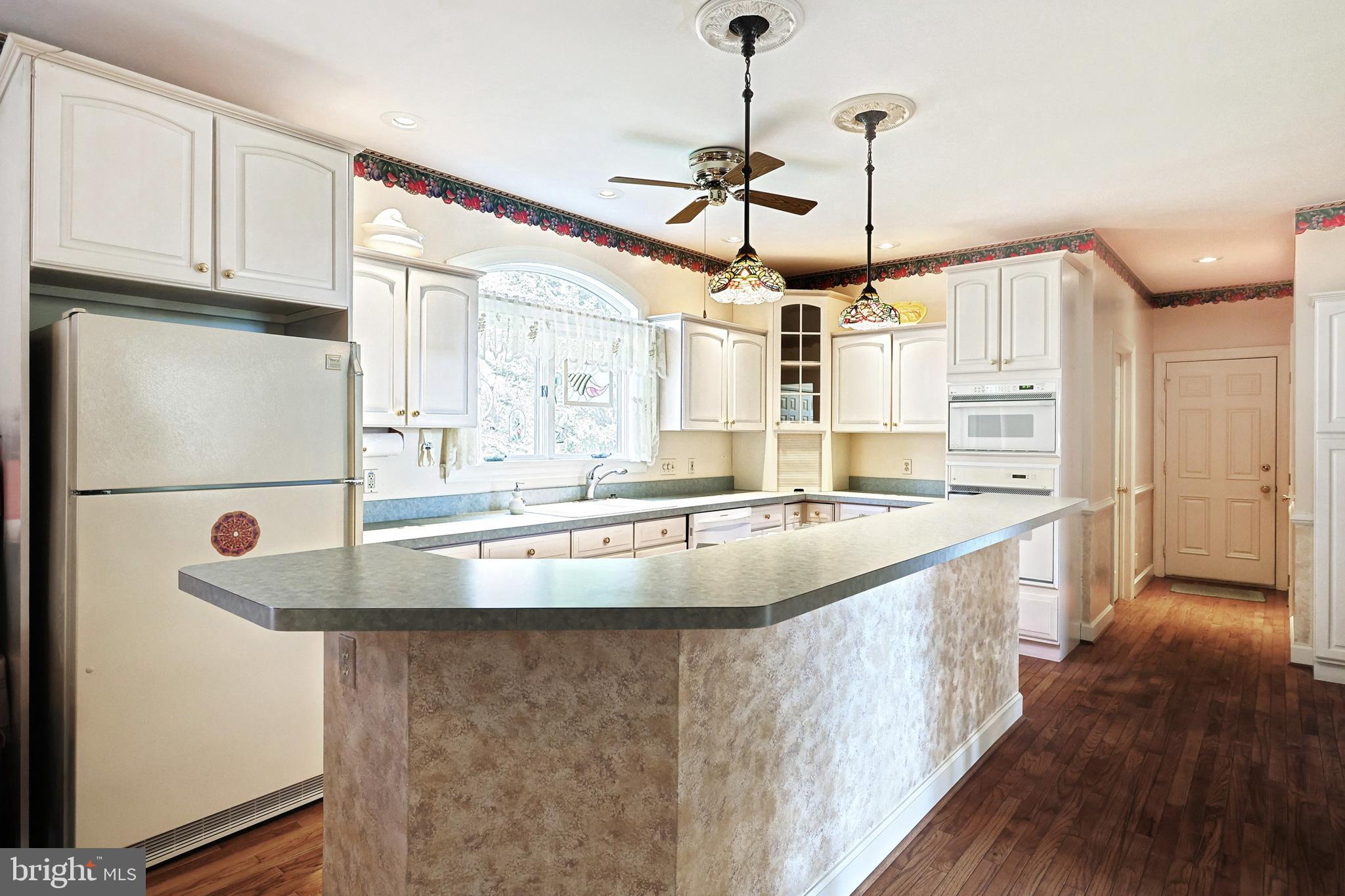 Kitchen with white paneled cabinets, a large peninsula, arched window, and stained-glass pendant lights.