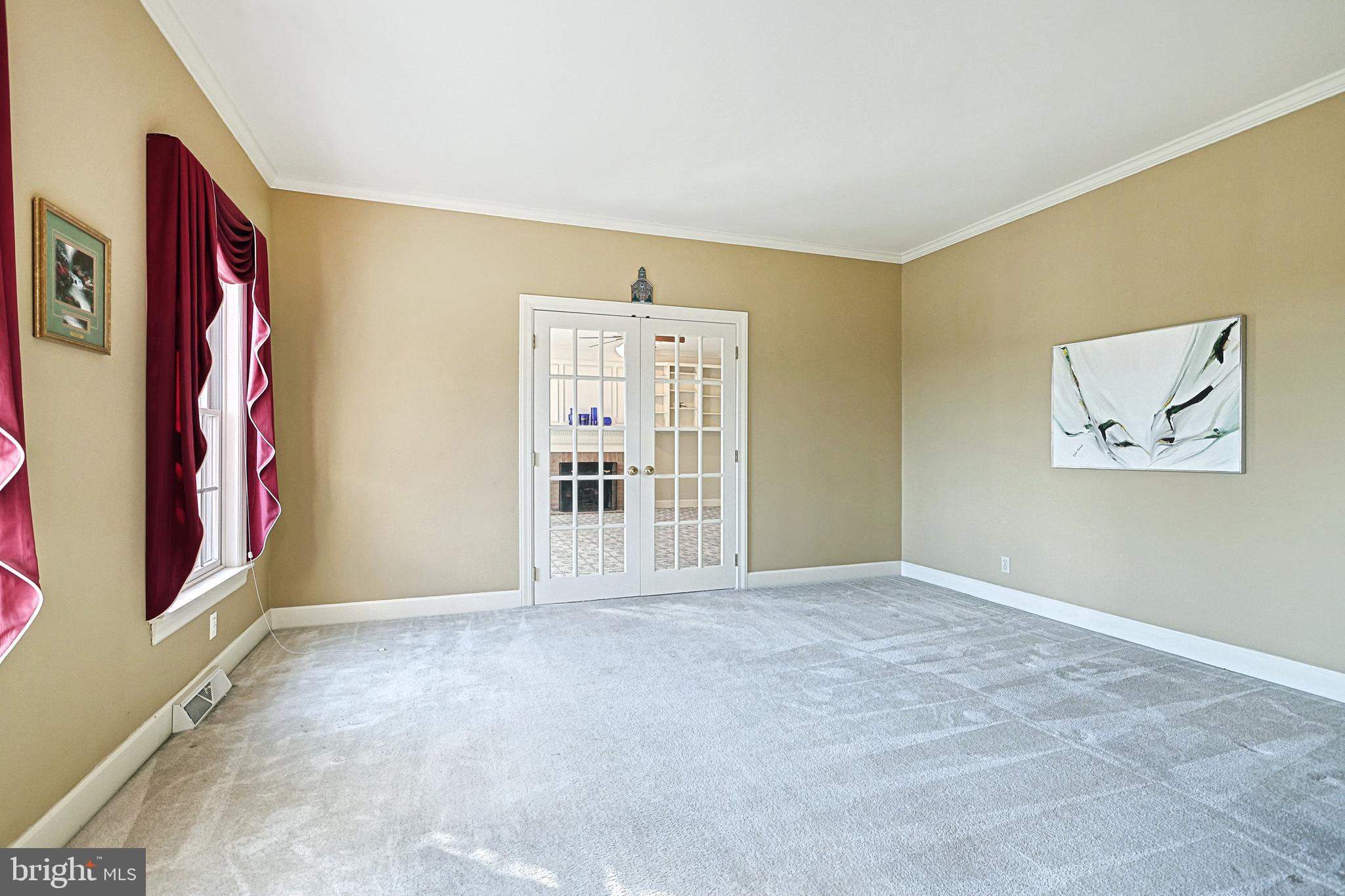Vacant carpeted room with burgundy curtains and glass-paneled French doors.