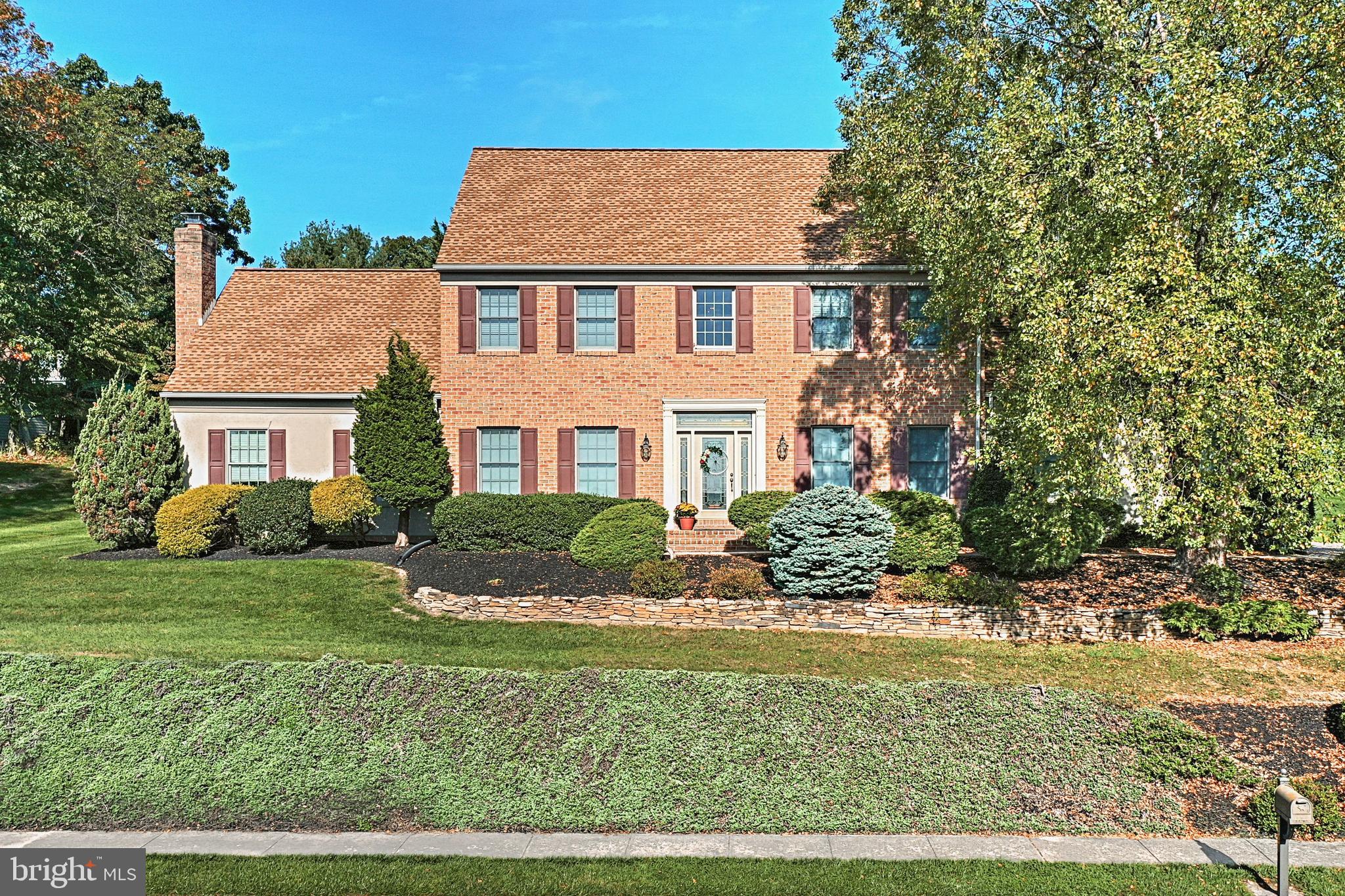 Two-story brick home with a landscaped front yard, mature trees, and a low stone retaining wall.