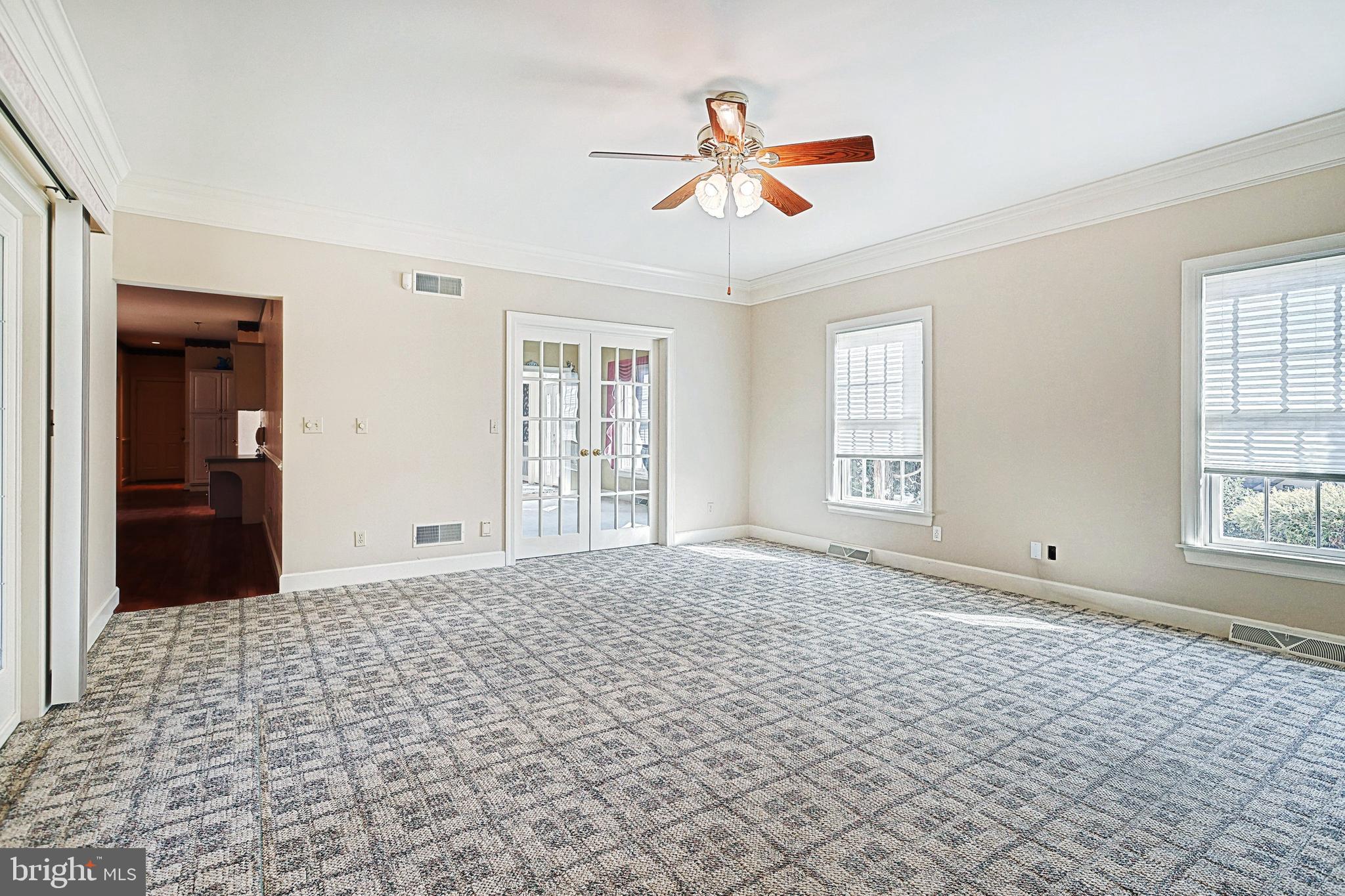 Empty carpeted living room with French doors, two windows, and a ceiling fan.