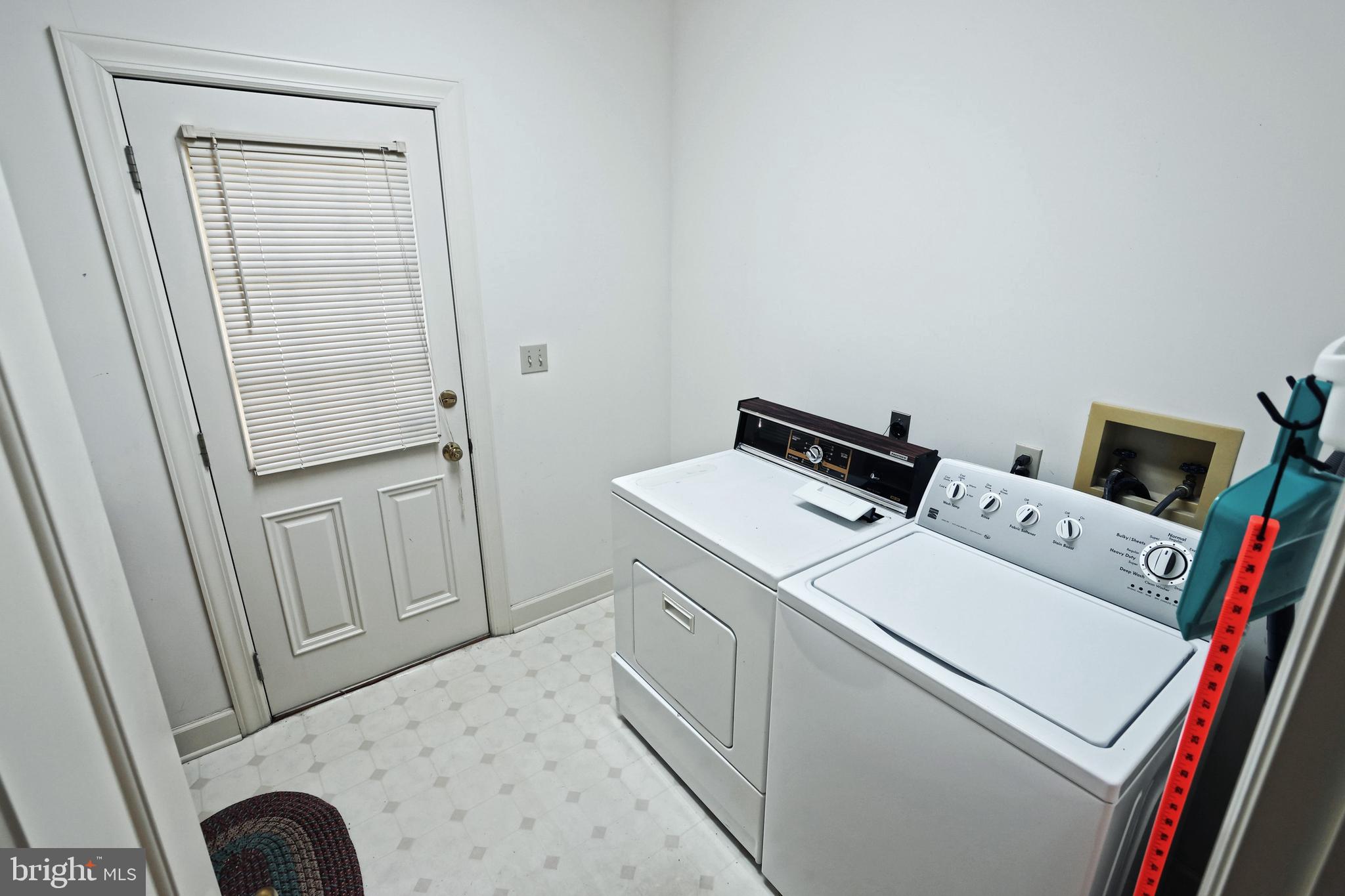 Laundry room with a white washer and dryer beside a paneled door with blinds.