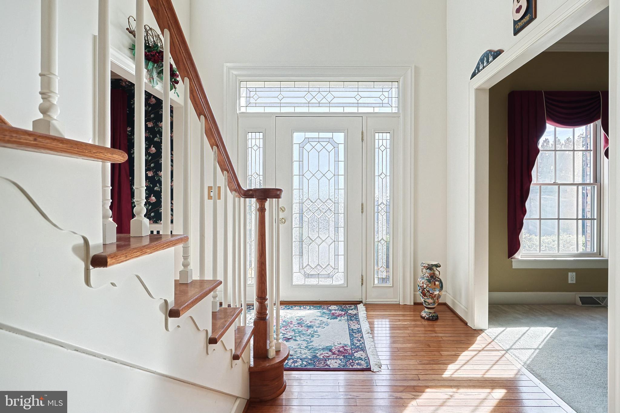 Foyer with a wood-railed staircase, hardwood floors, and a decorative glass front door.