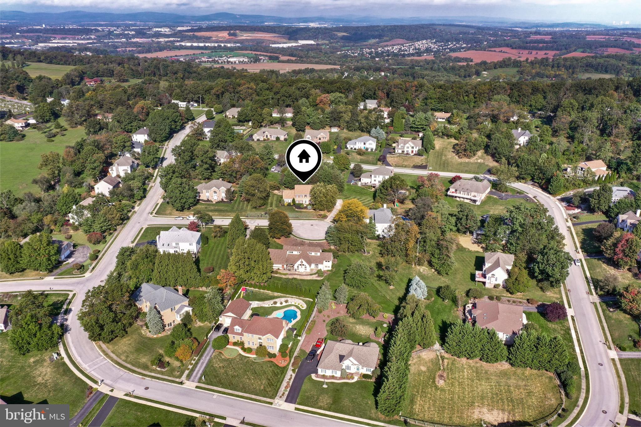 Aerial view of a leafy neighborhood, with a map pin marking a house among curving streets and lawns.