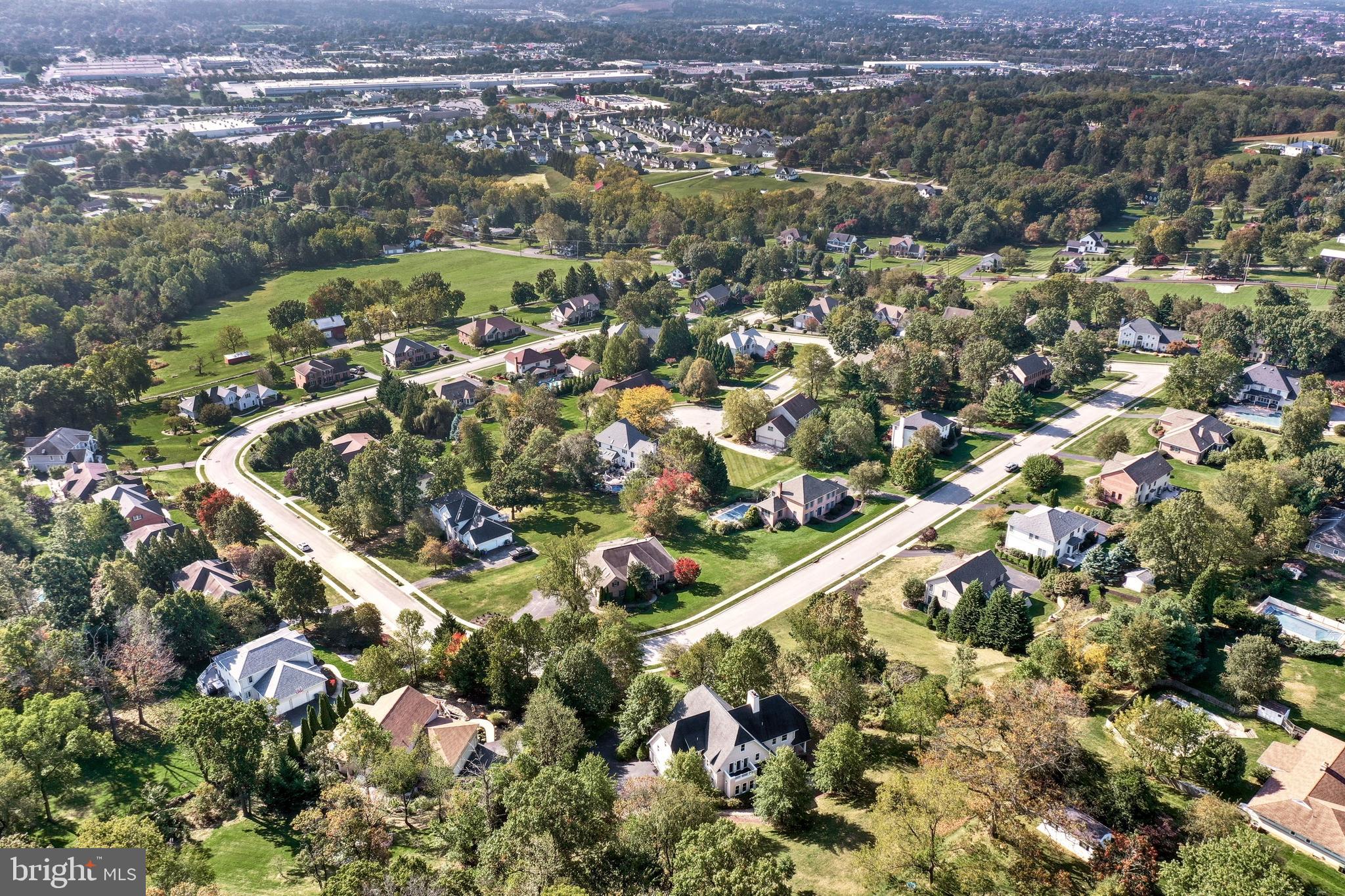 Aerial view of a leafy residential neighborhood with curving streets, detached homes, and wooded surroundings.