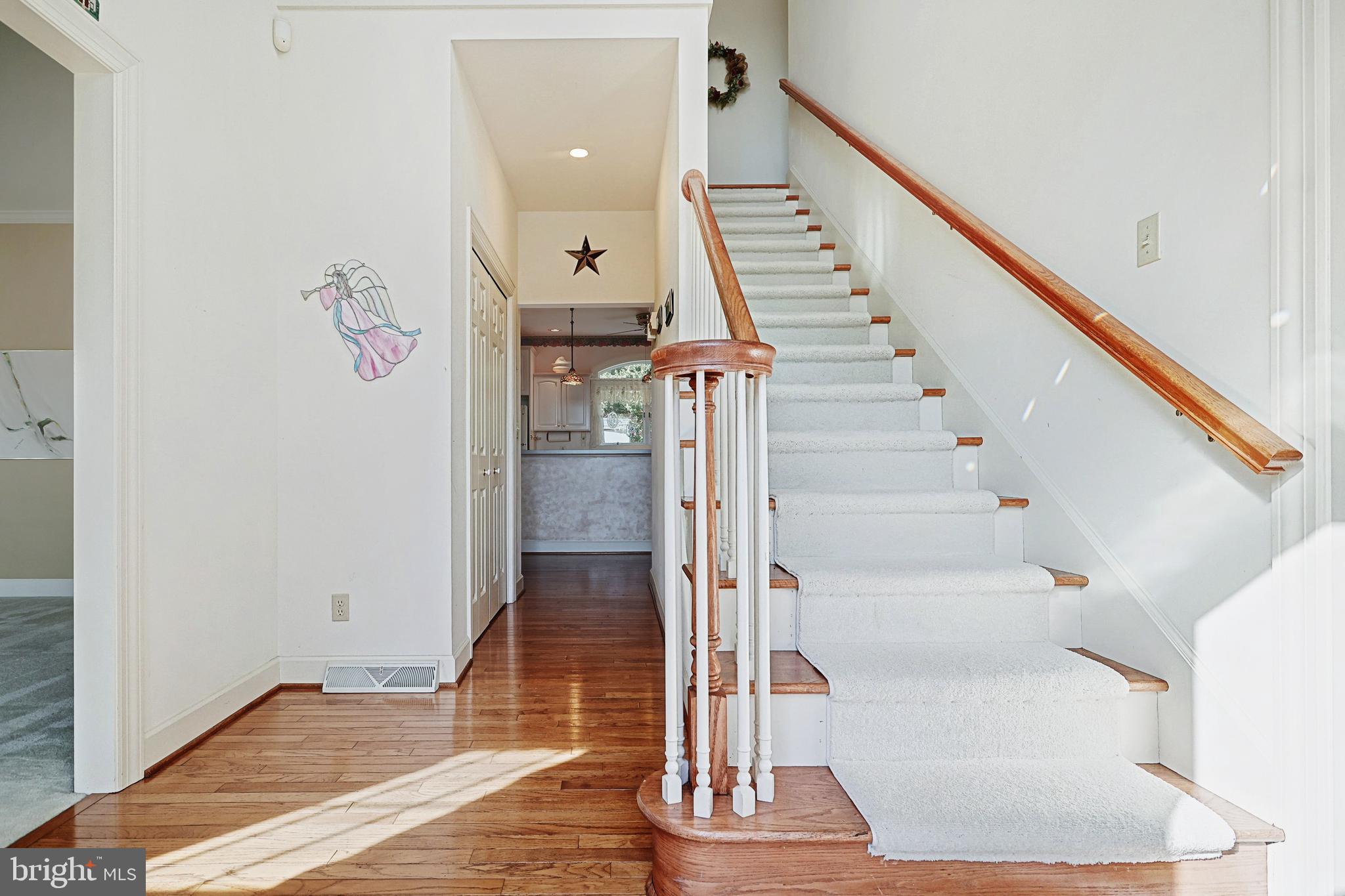Foyer with a carpeted staircase, polished wood railings, and hardwood floors.