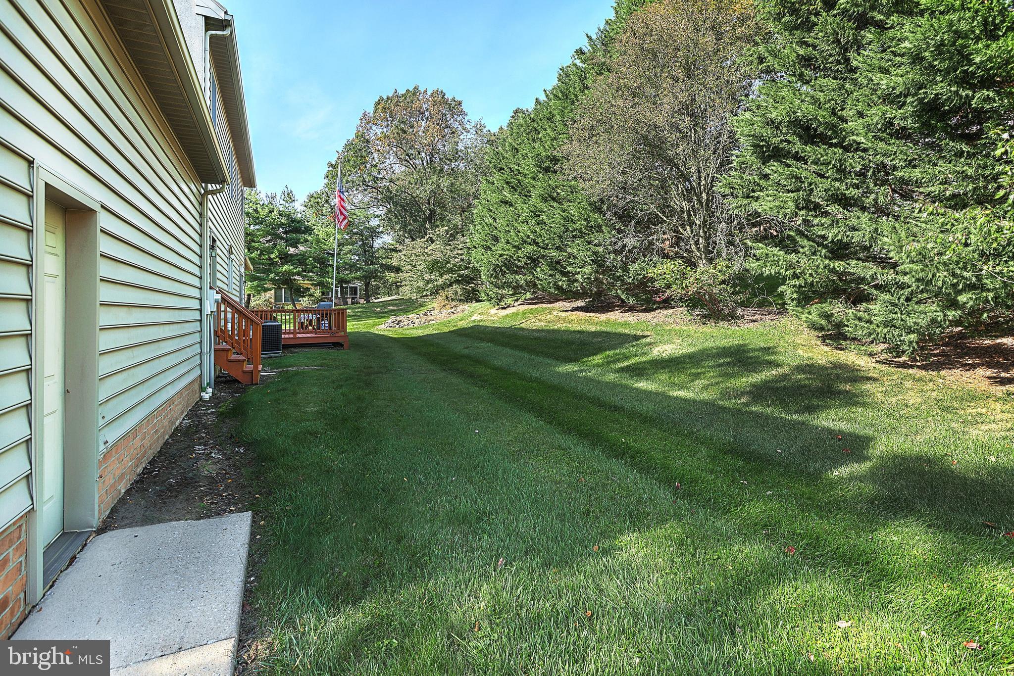 Home’s side yard with a broad lawn, small wooden deck, mature trees, and an American flag.