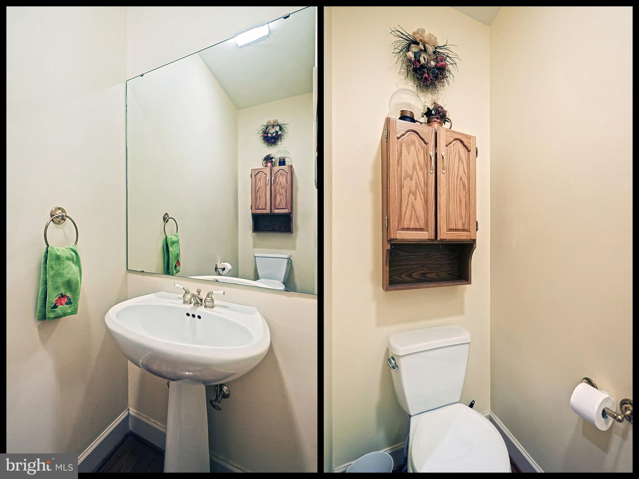 Powder room with a pedestal sink, large mirror, toilet, and wooden wall cabinet.