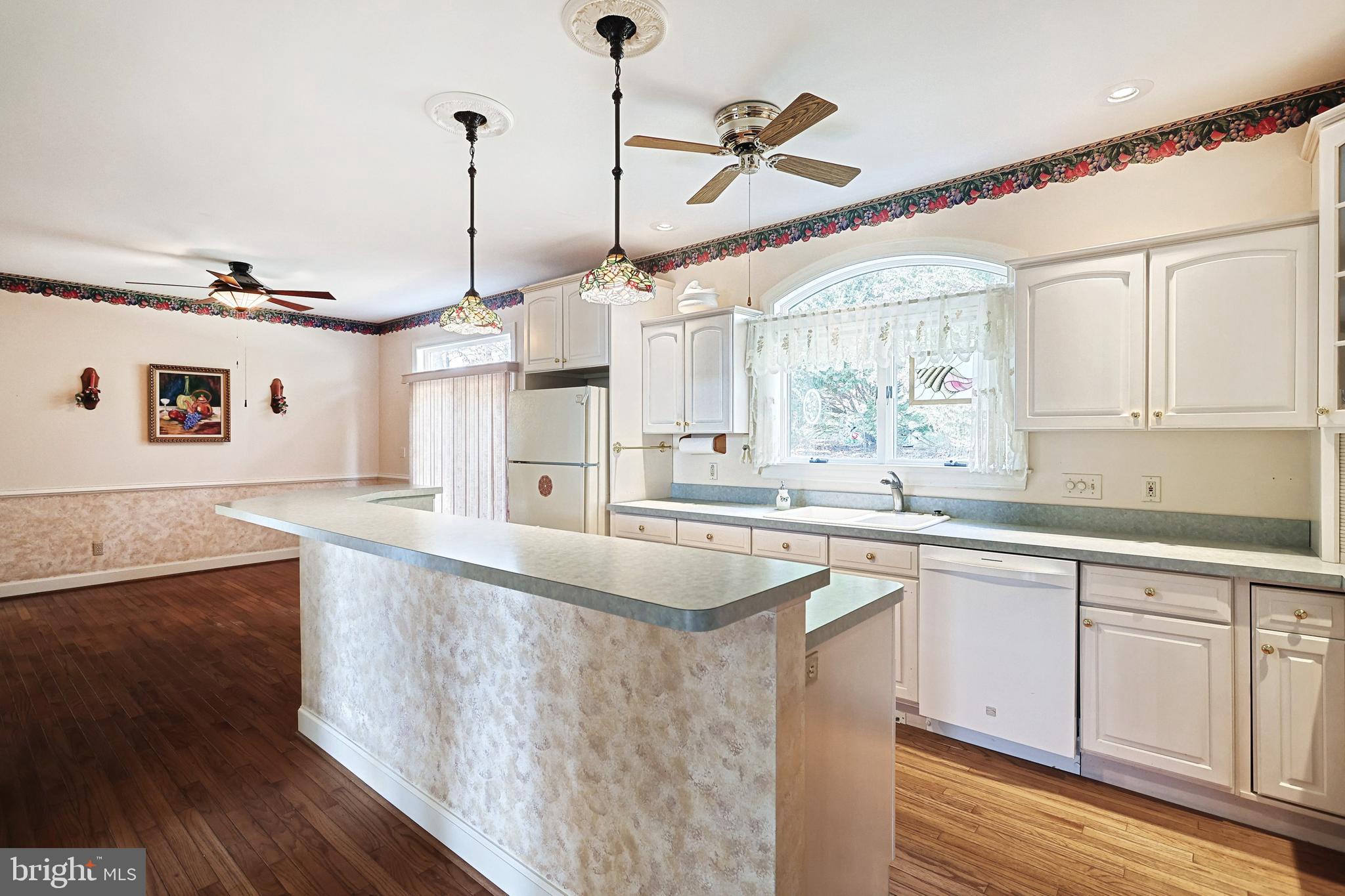 Kitchen with a large peninsula island, white cabinets, window-side sink, and dark hardwood floors.