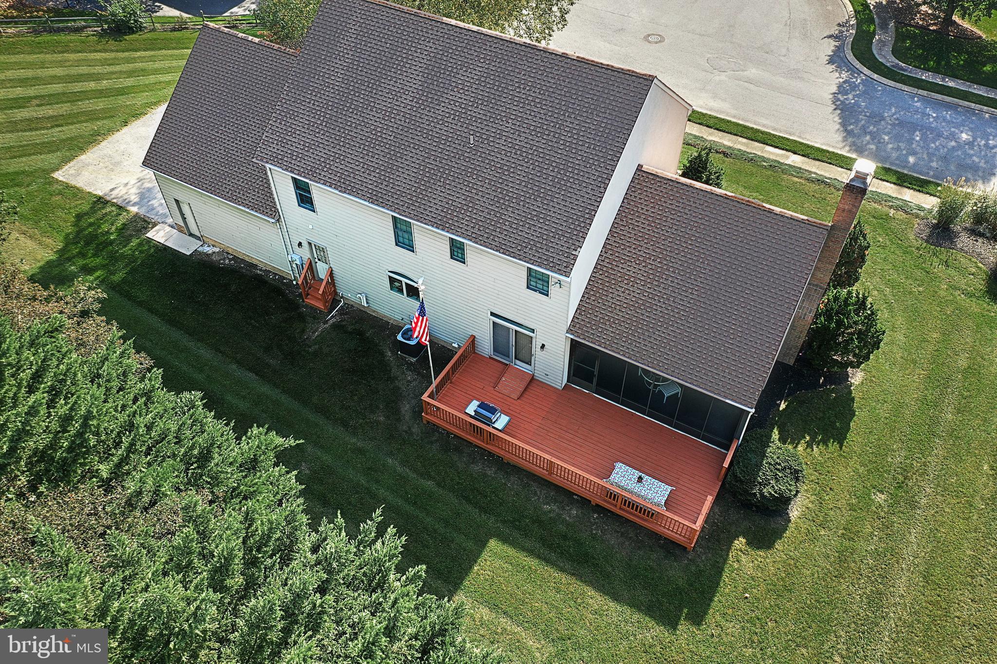 Aerial view of a two-story home’s rear deck and screened porch, surrounded by a large green lawn.