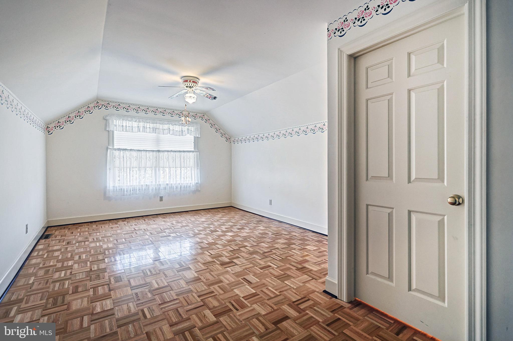 Empty bedroom with patterned parquet flooring, a sloped ceiling, and floral wall borders.