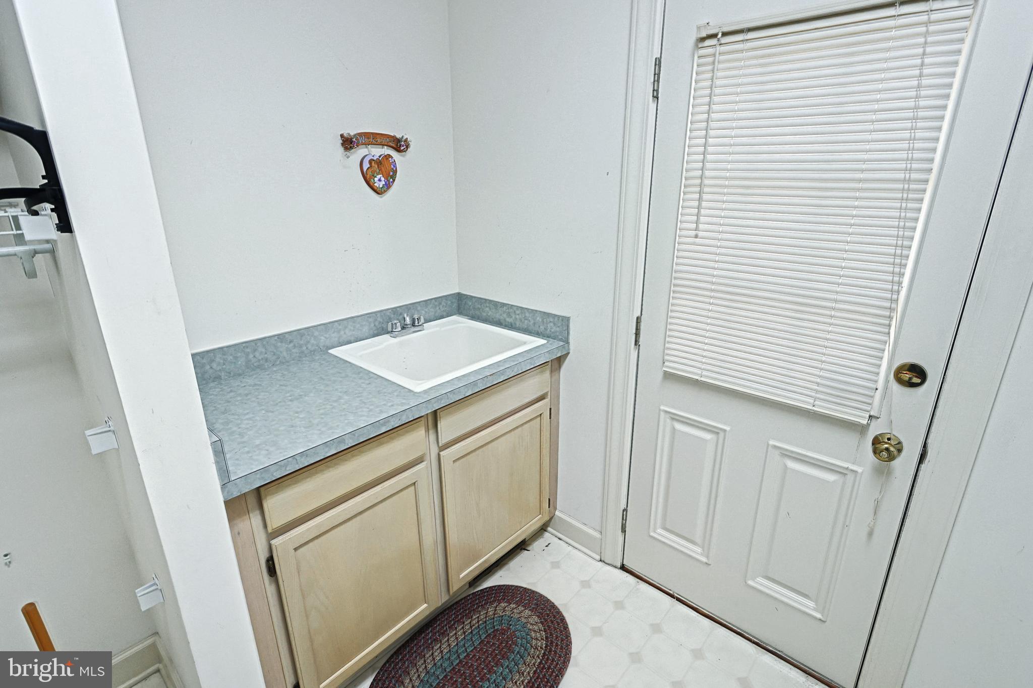 Bathroom vanity with a white sink and gray countertop beside a door with blinds.