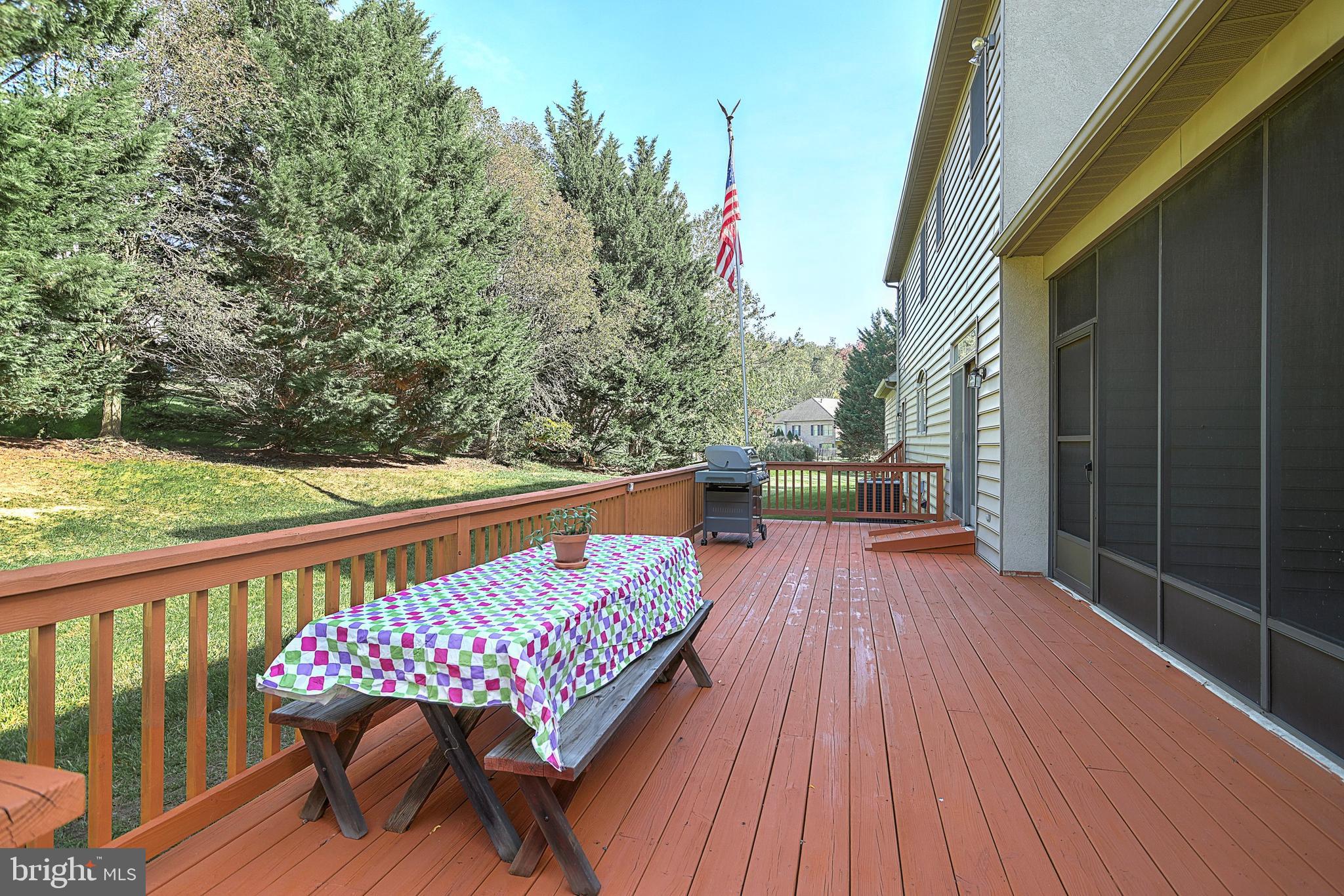 Raised deck with a colorful picnic table and grill overlooking a tree-lined yard.