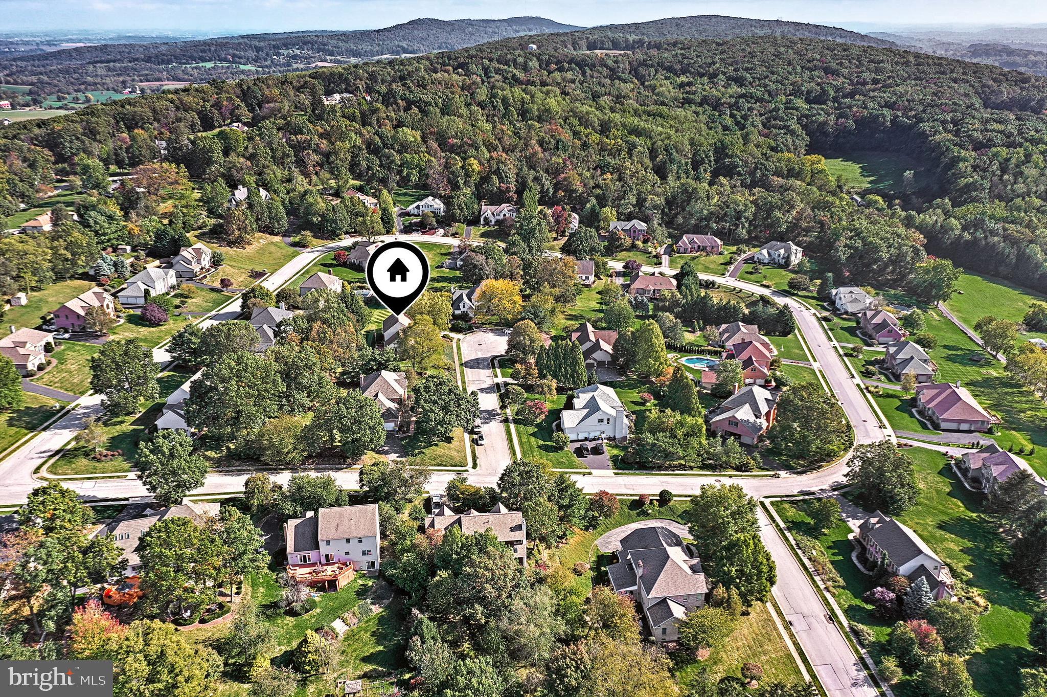 Aerial view of a leafy neighborhood, with a home marker among houses and wooded hills.