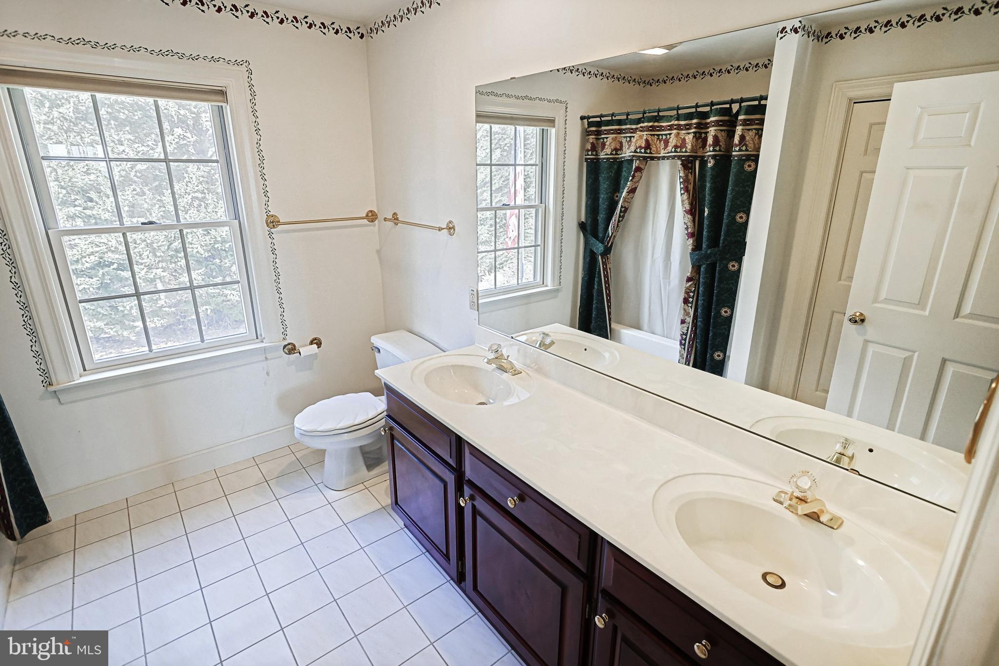 Bathroom with a double-sink vanity, large mirror, tiled floor, and curtained bathtub.