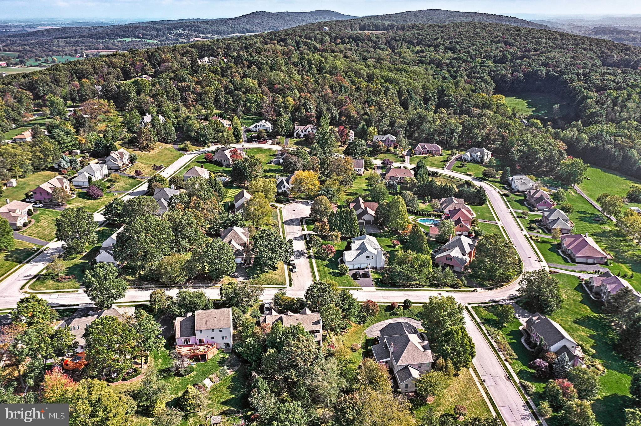 Aerial view of homes along curved neighborhood streets, with wooded hills in the background.