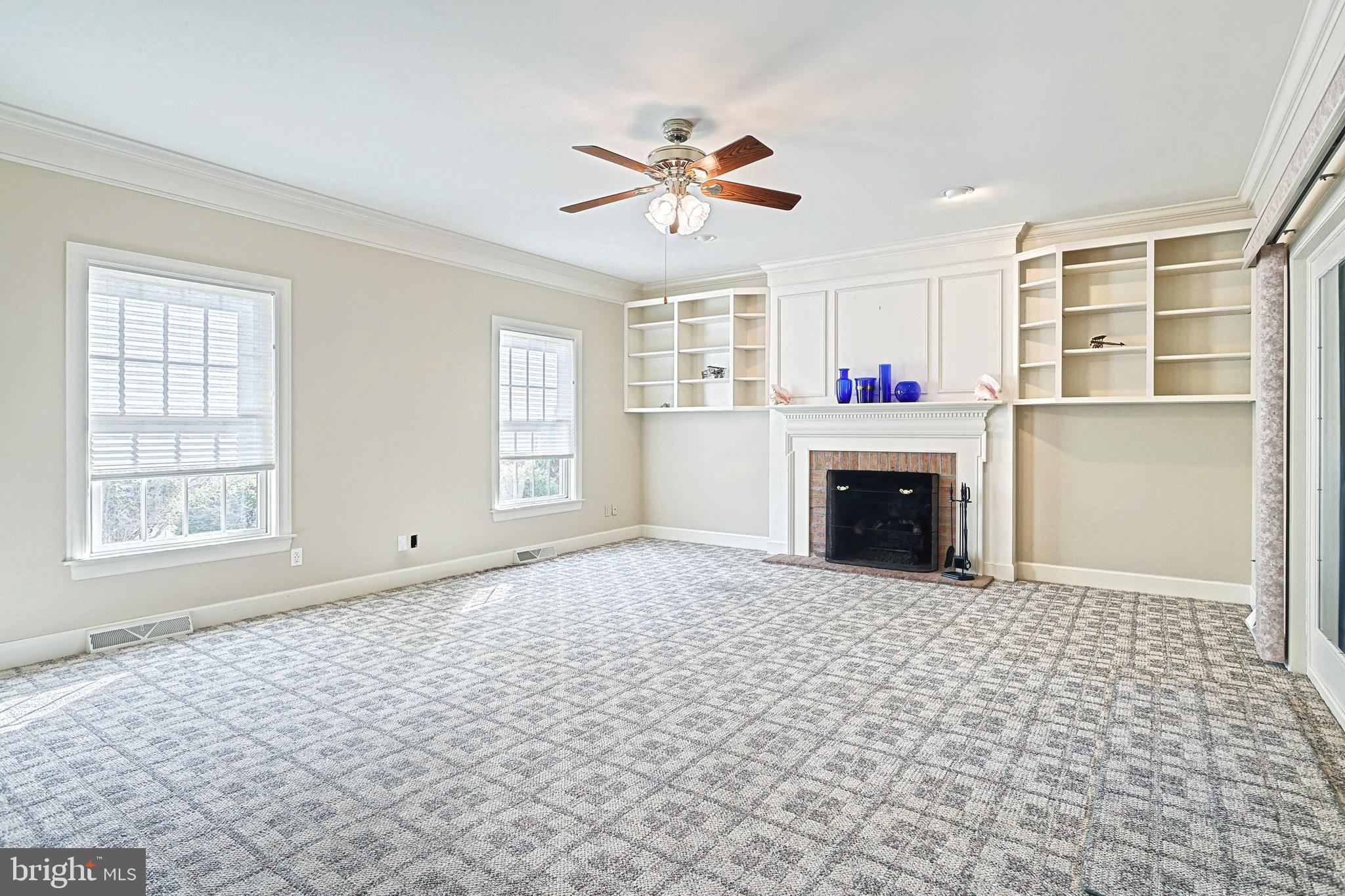 Unfurnished living room with patterned carpet, built-in shelving, and a white fireplace.