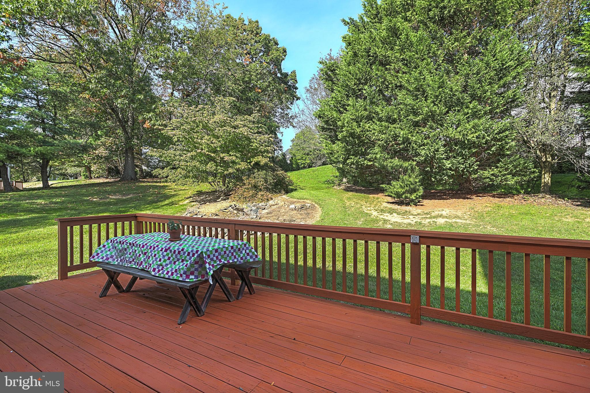 Wood deck with a picnic table overlooking a tree-lined backyard and grassy slope.