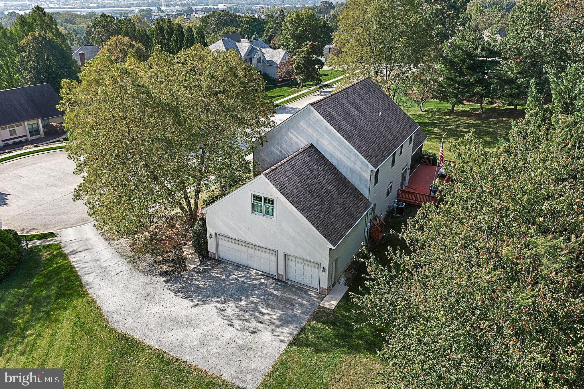 Aerial view of a two-story home with attached garages, red deck, and mature trees.