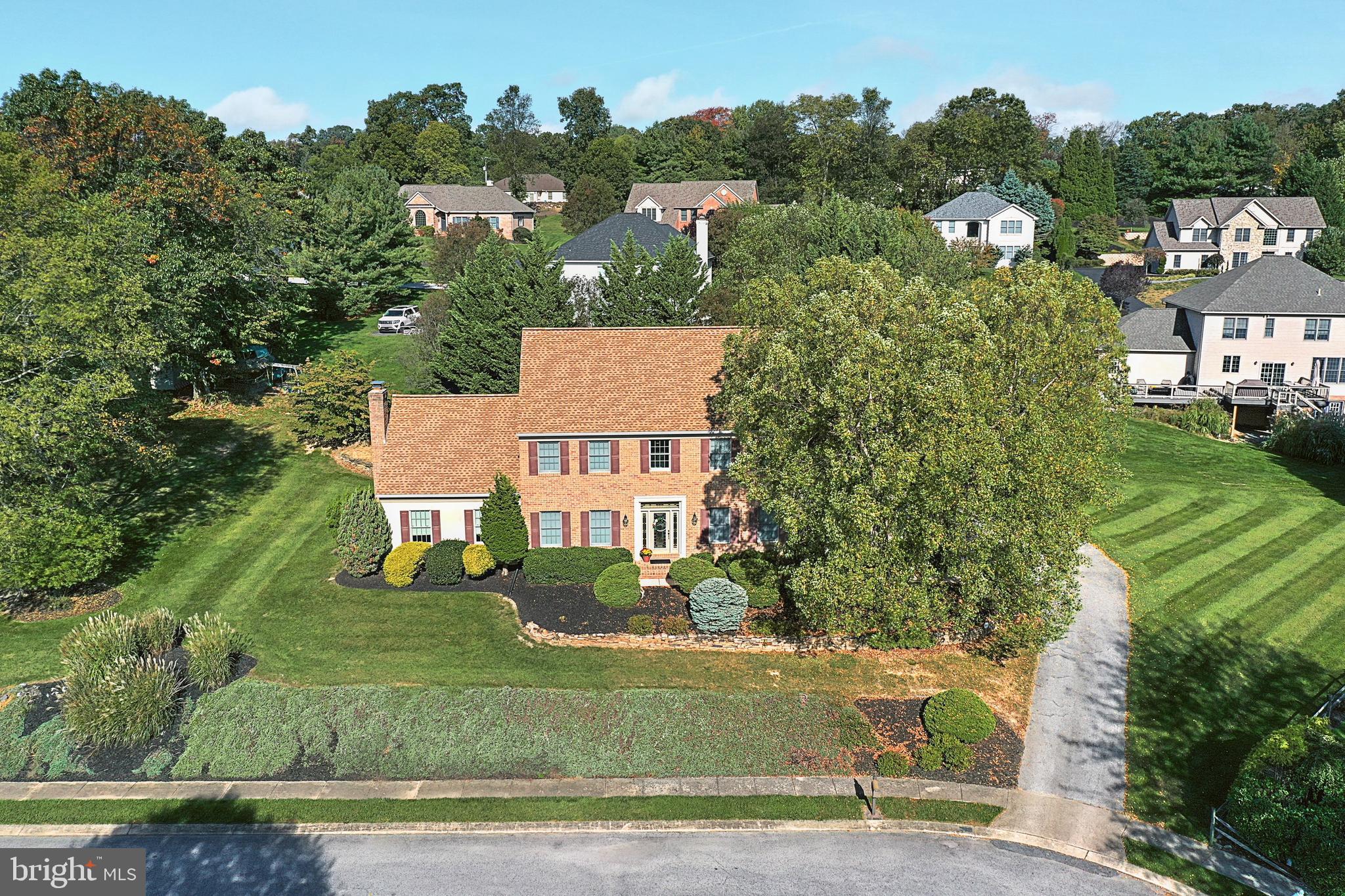 Aerial view of a brick two-story home with a landscaped yard and mature trees.