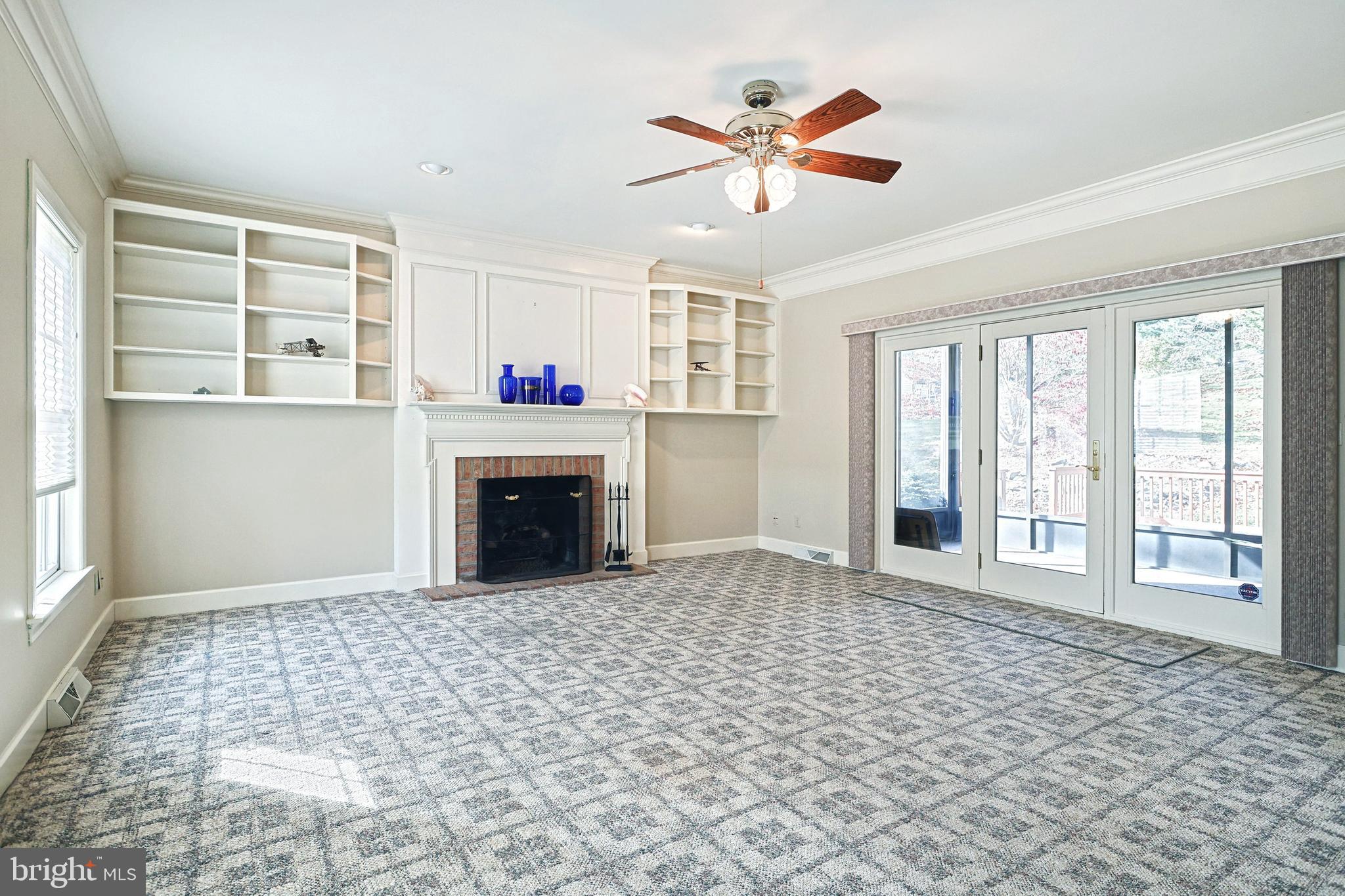 Living room with built-in shelves, a brick fireplace, patterned carpet, and glass doors to a deck.