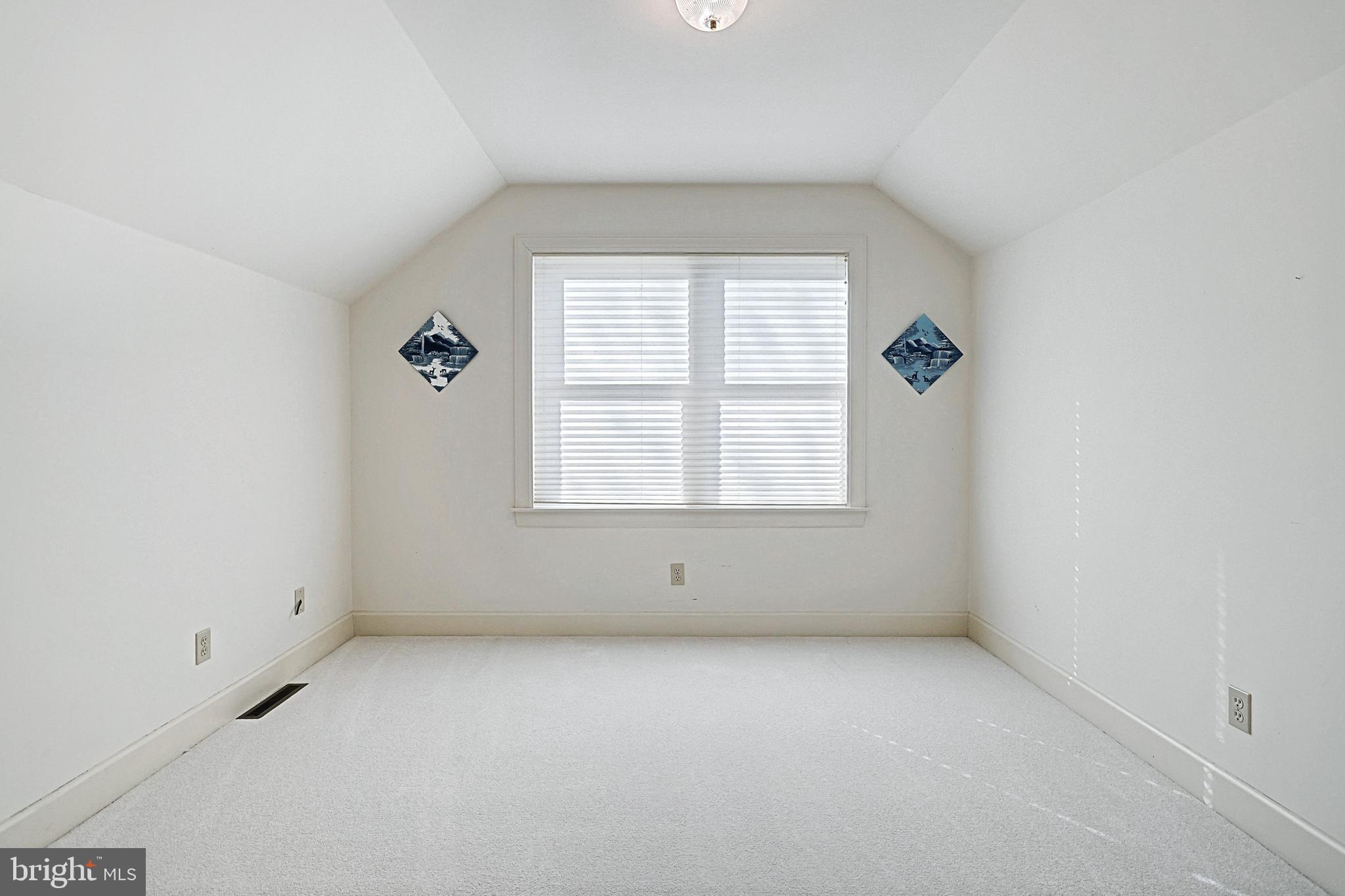 Empty carpeted room with a sloped ceiling, window blinds, and two wall pictures.