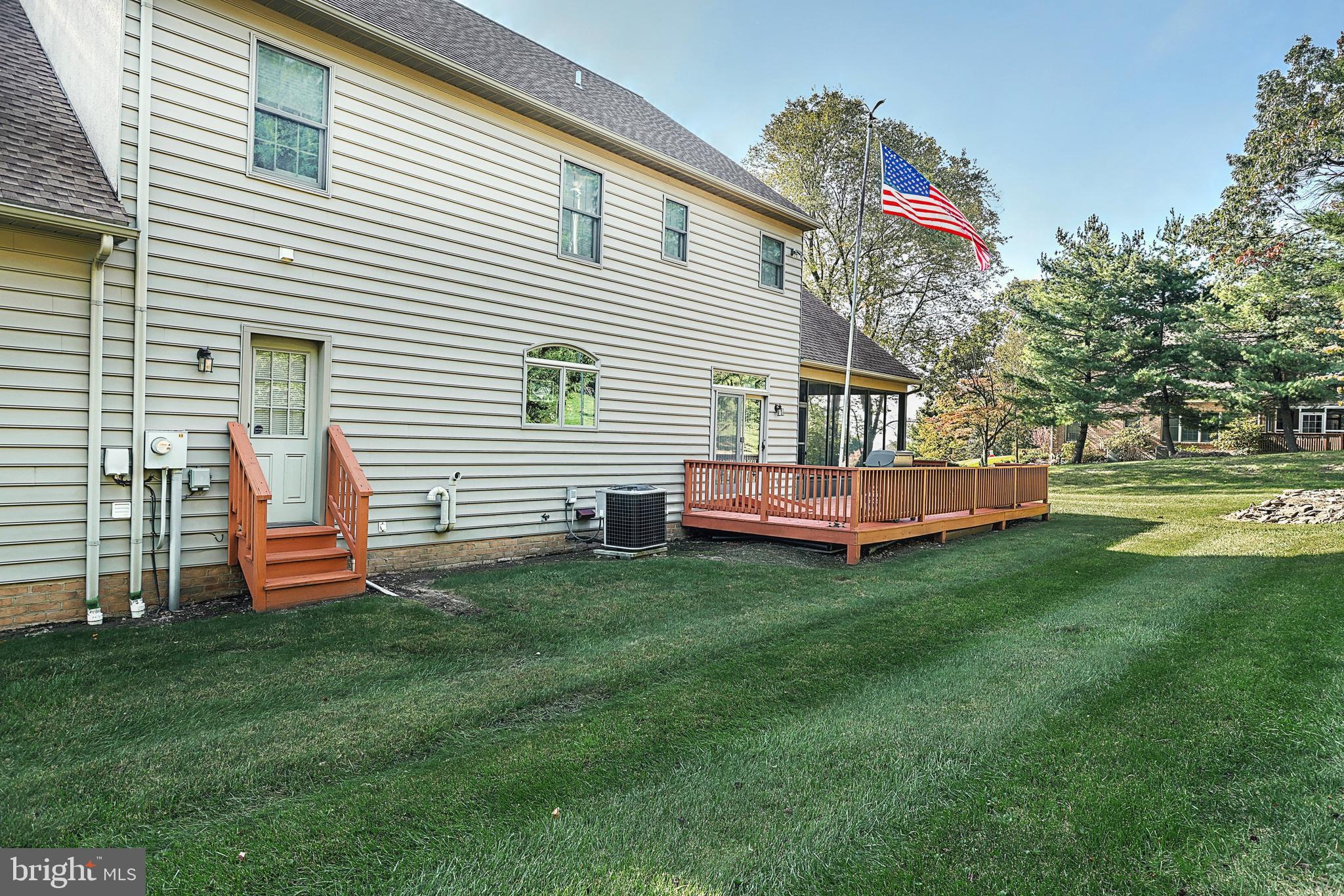 Two-story home's rear exterior with a raised wooden deck, broad lawn, and American flag.