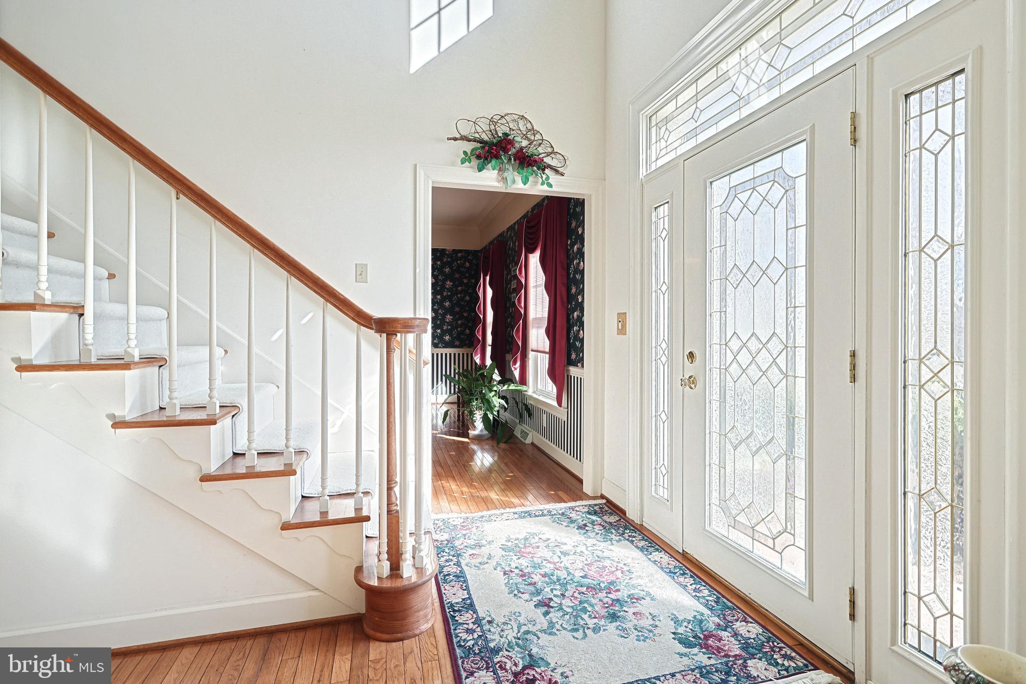 Foyer with a white staircase, patterned rug, and decorative glass front door.