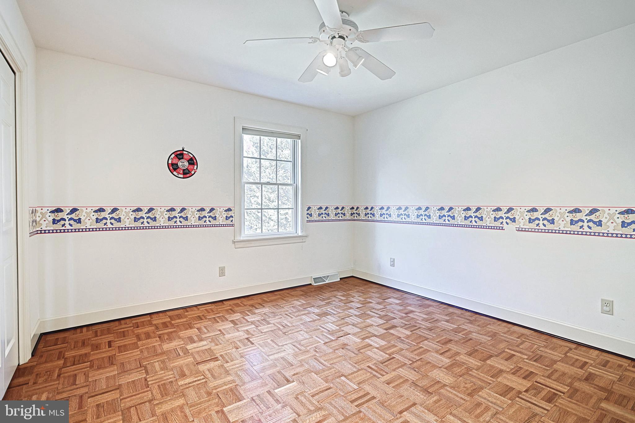 Empty bedroom with parquet flooring, a ceiling fan, and a playful wallpaper border.