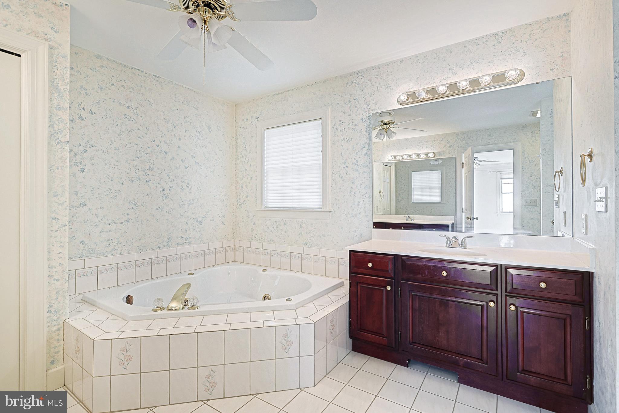 Bathroom with a corner jetted tub, dark wood vanity, and large mirror.