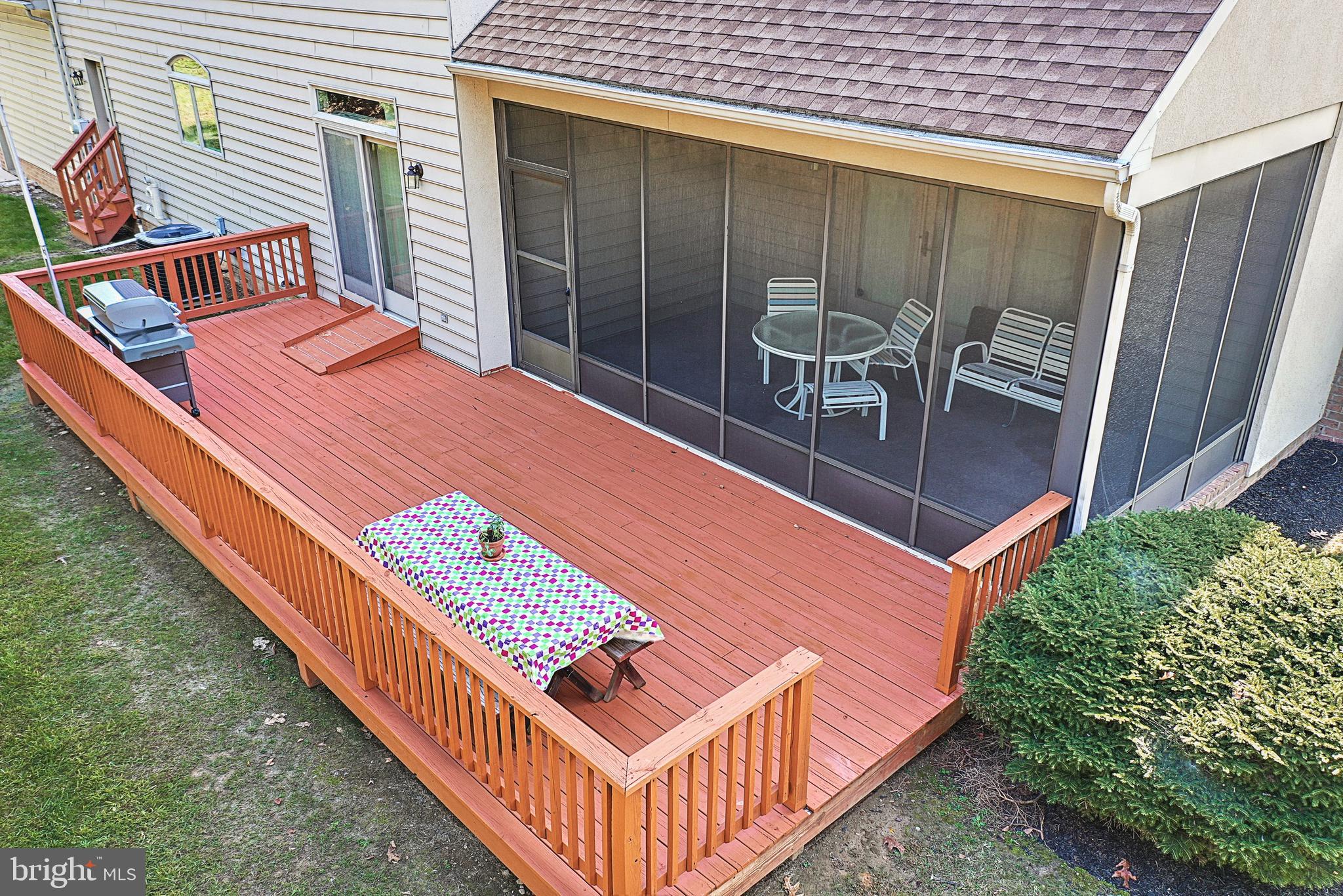 Wood deck with a barbecue grill and screened porch furnished with a round table and chairs.