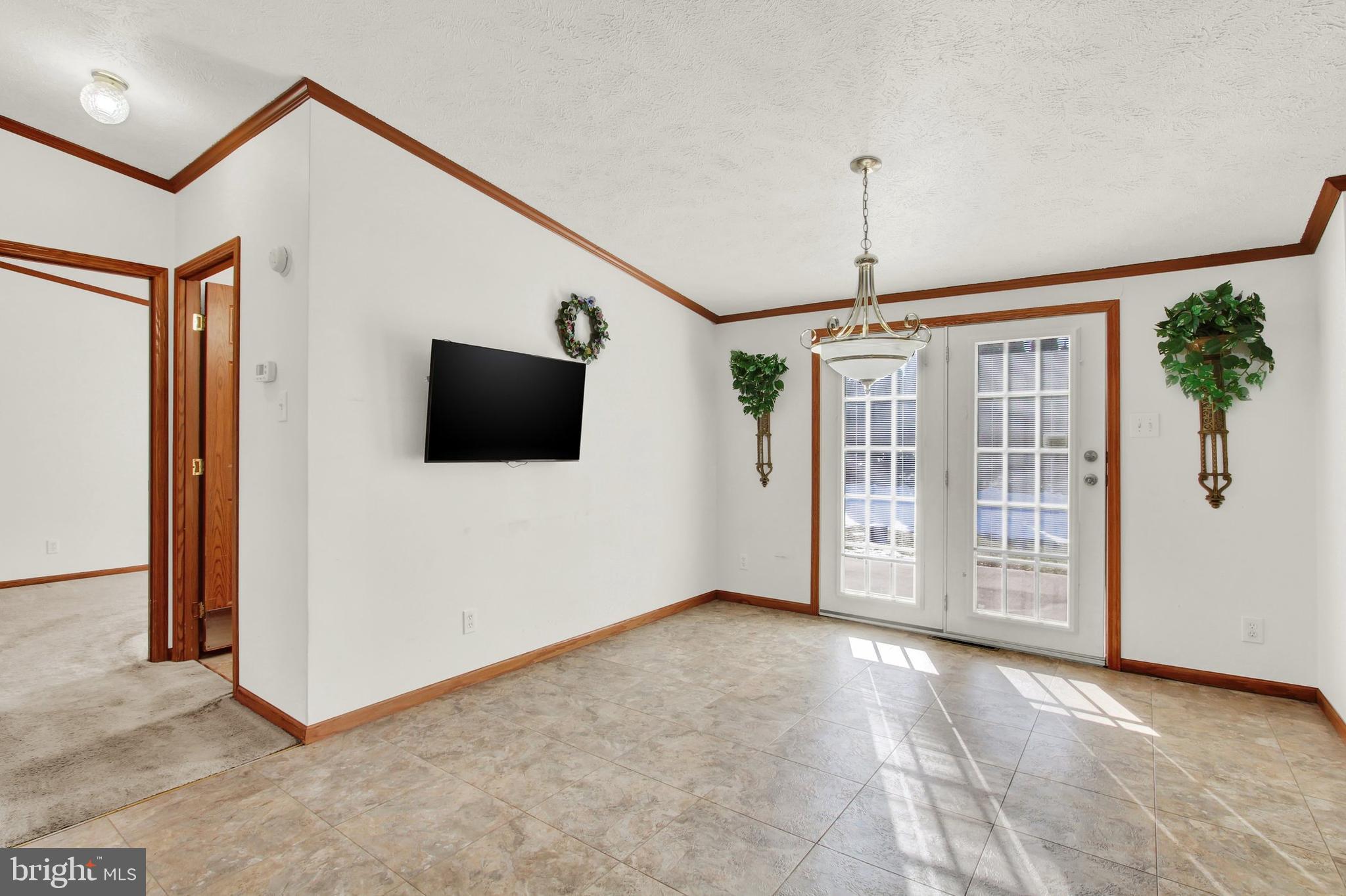 Tiled living area with wood trim, a wall-mounted television, and French doors to a patio.