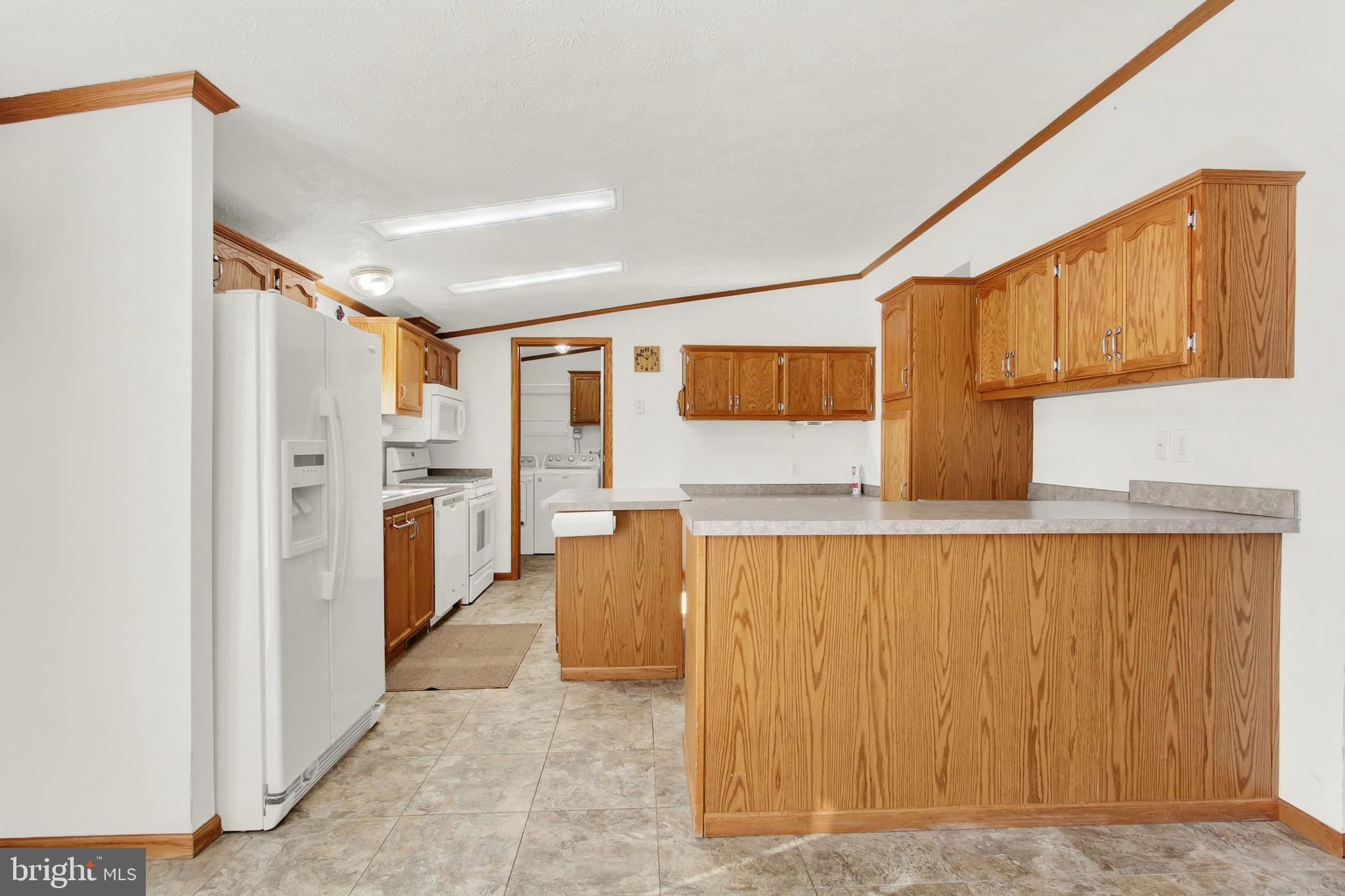Kitchen with extensive honey-colored wood cabinetry, a large peninsula, white appliances, and tile flooring.