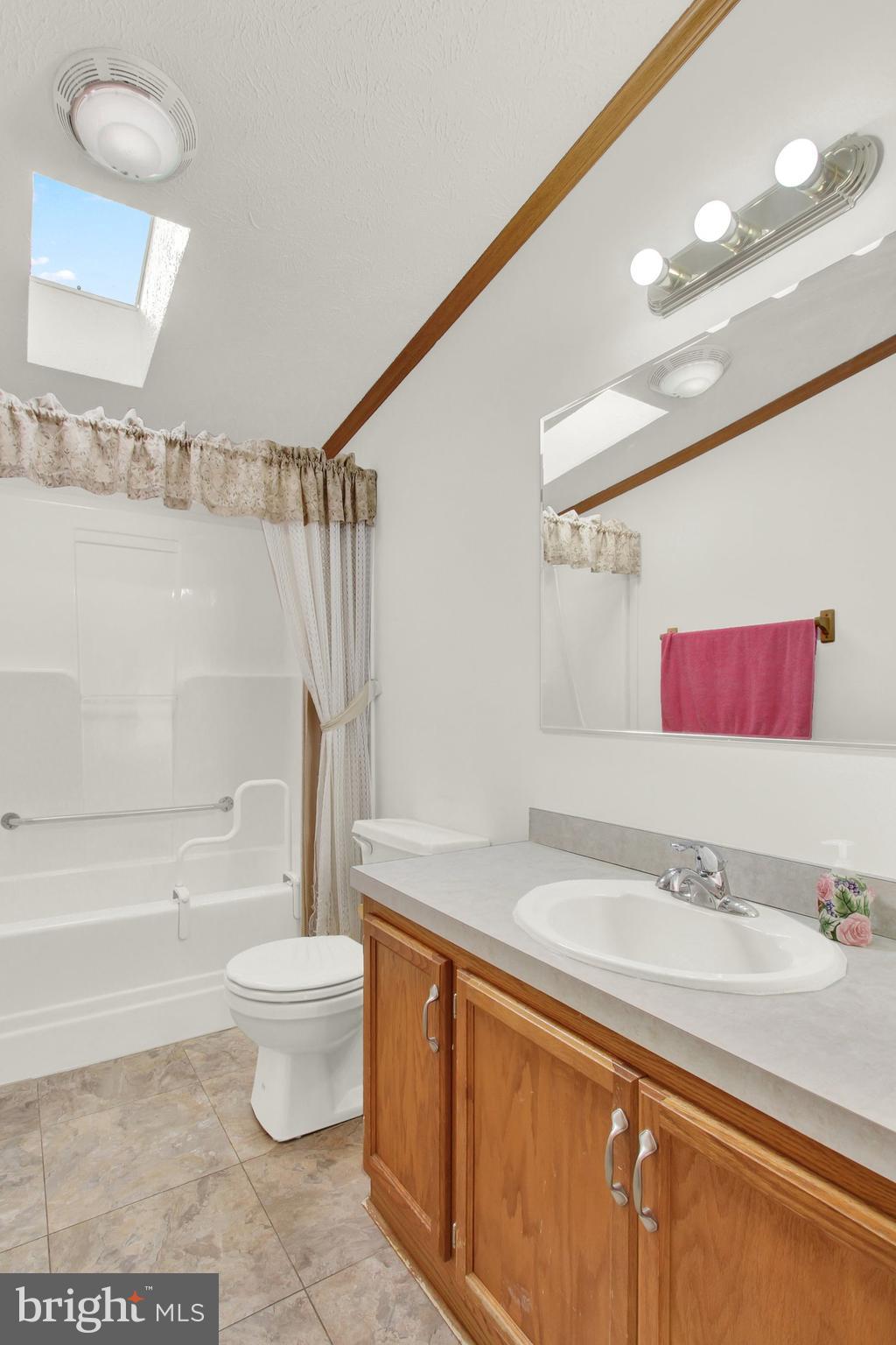 Bathroom with wood vanity, oval sink, tub and shower, and a skylight.