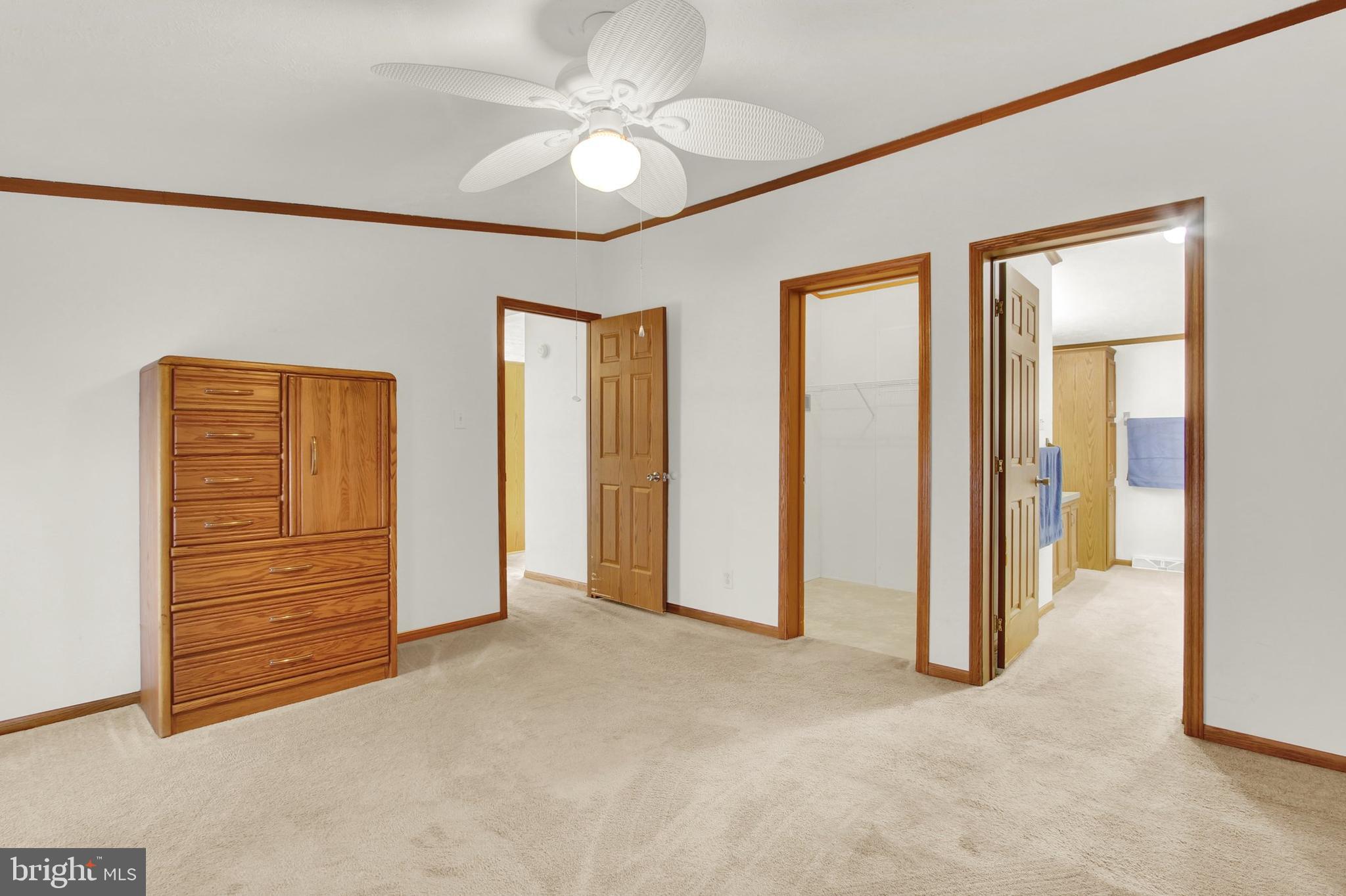 Carpeted bedroom with a wooden dresser, ceiling fan, and open doorways to adjoining rooms.