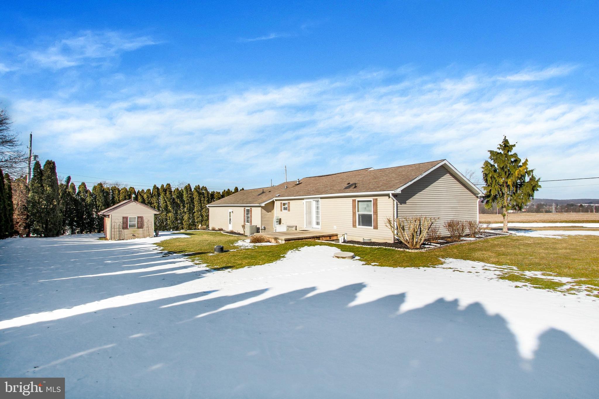 Beige single-story home with a small deck and detached shed in a snow-covered yard.