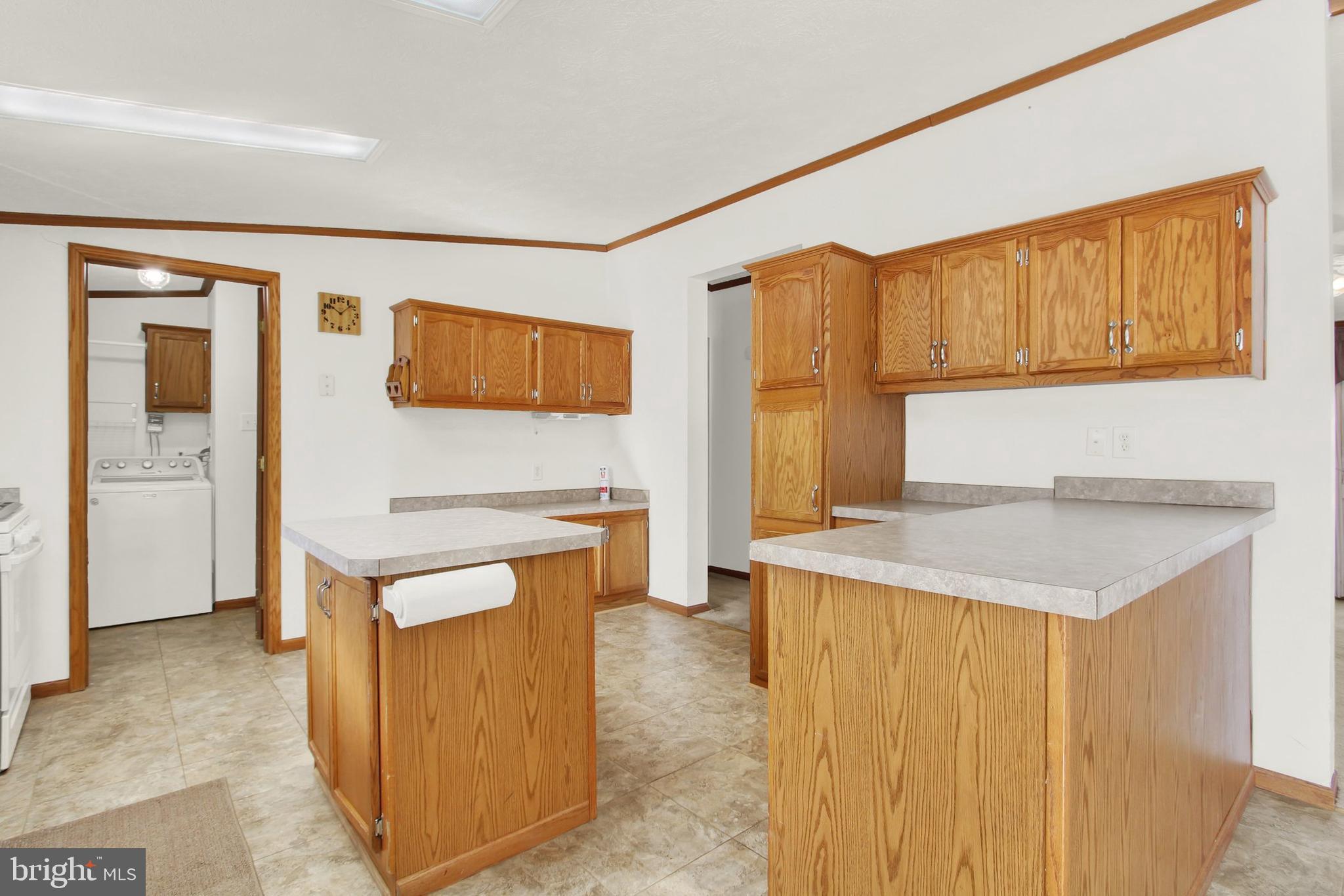 Kitchen with honey-colored wood cabinets, two peninsula counters, and a washer visible through the doorway.